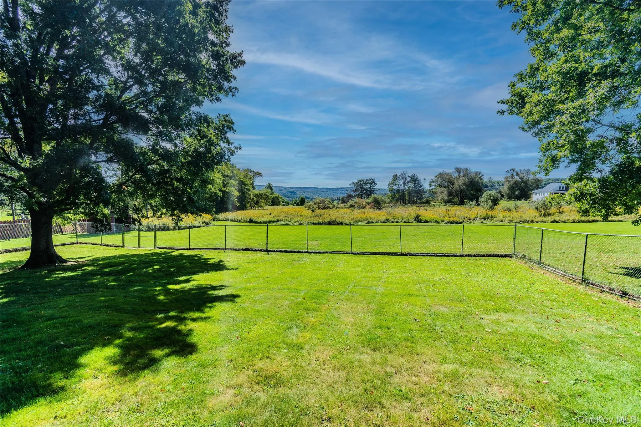 Expansive green space featuring chain-link fencing and mature trees Expansive green space featuring chain-link fencing and mature trees