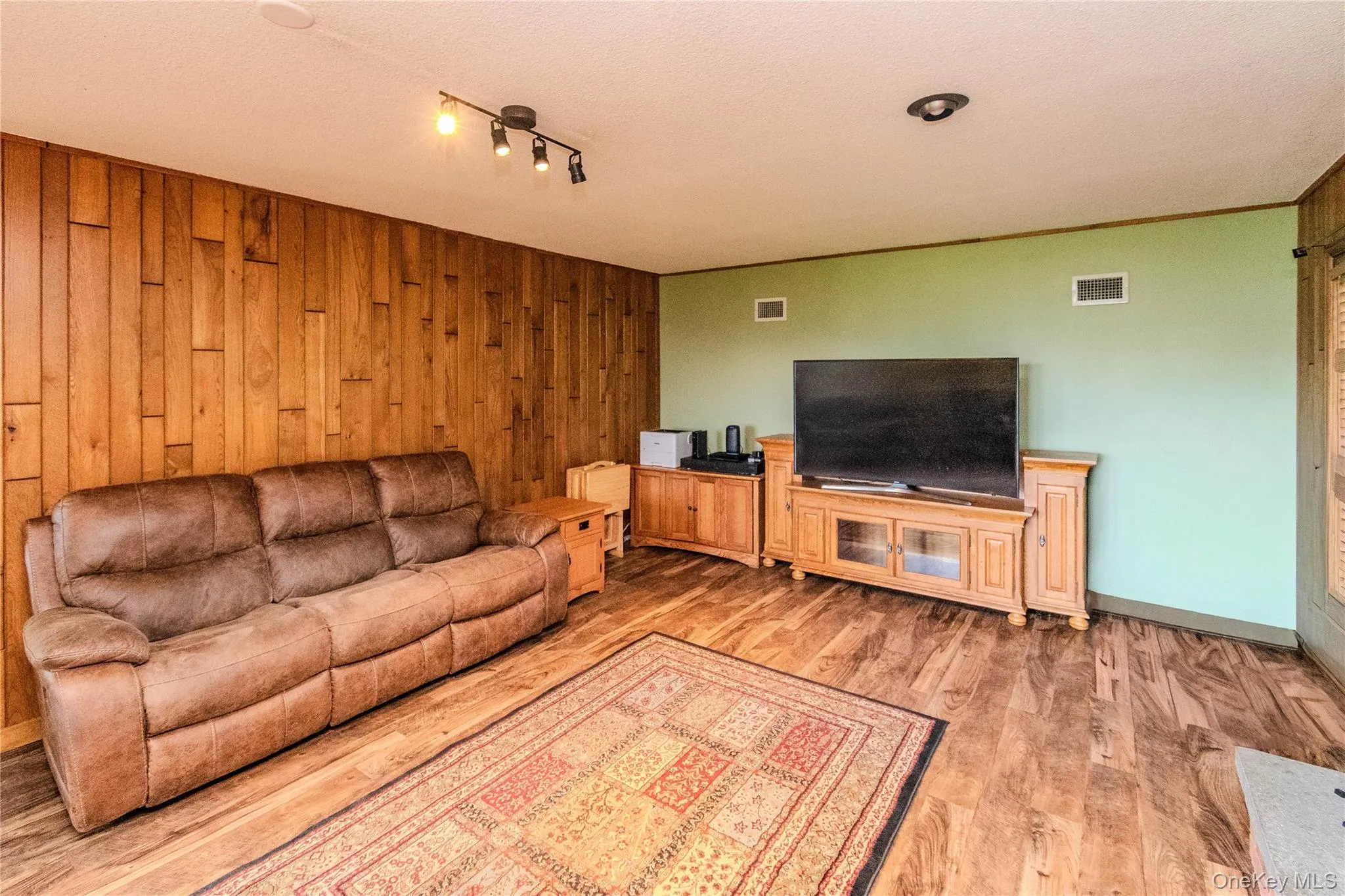 Wood-paneled accent wall, wood-finish flooring, recessed ceiling lighting, and track lighting fixture Wood-paneled accent wall, wood-finish flooring, recessed ceiling lighting, and track lighting fixture