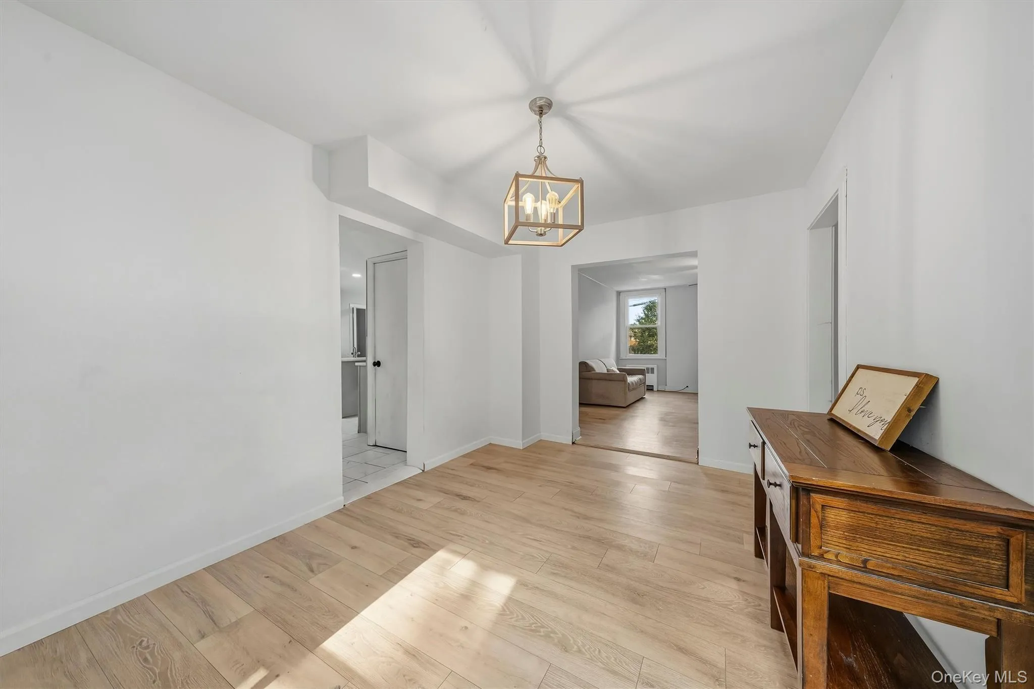 Wood-finish flooring throughout, a modern chandelier, and bright white wall finishes Wood-finish flooring throughout, a modern chandelier, and bright white wall finishes