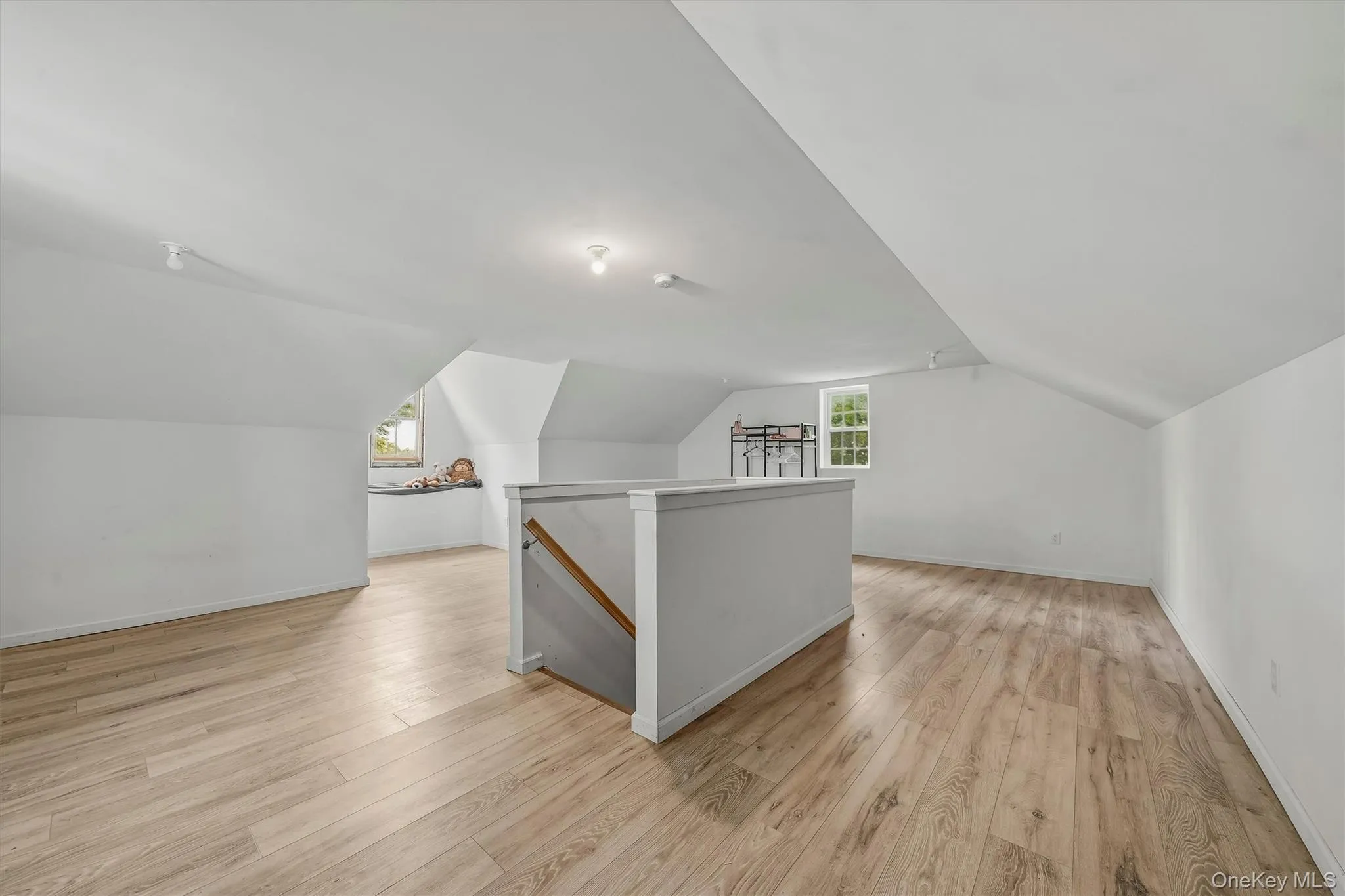 Expansive attic space featuring wood-finish flooring, sloped ceilings, multiple windows, and track lighting Expansive attic space featuring wood-finish flooring, sloped ceilings, multiple windows, and track lighting