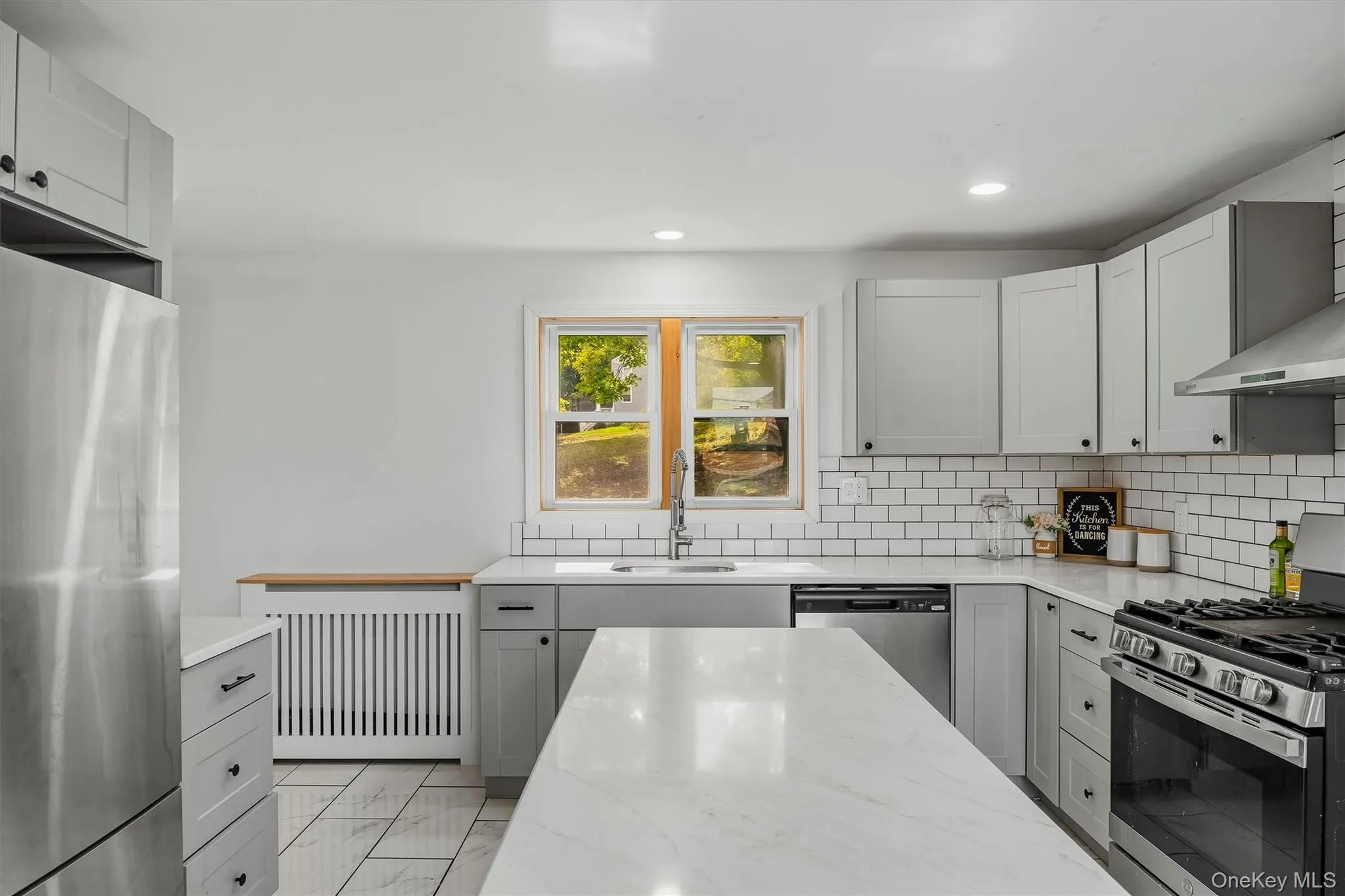 Modern kitchen with light grey cabinetry, white subway tile backsplash, stainless steel appliances, and a central island with a white countertop Modern kitchen with light grey cabinetry, white subway tile backsplash, stainless steel appliances, and a central island with a white countertop