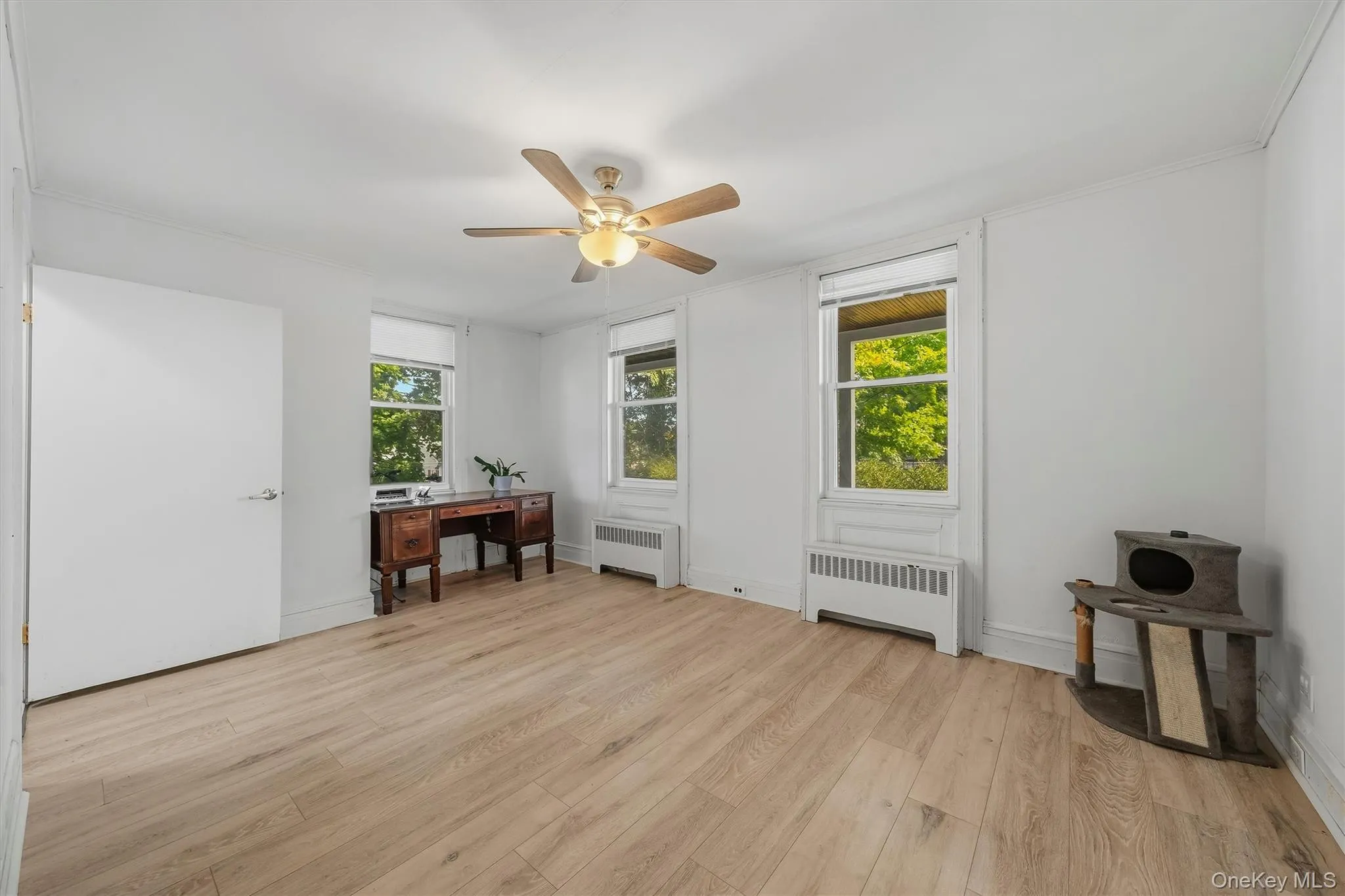 Wood-finish flooring, two windows with roller shades, white walls, and a ceiling fan with integrated lighting Wood-finish flooring, two windows with roller shades, white walls, and a ceiling fan with integrated lighting
