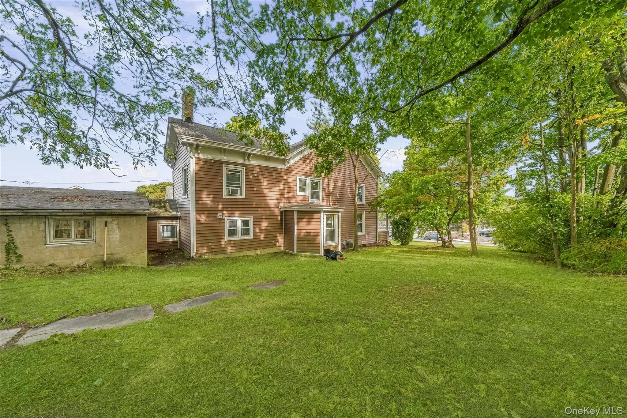 Expansive green lawn with mature trees and a multi-level structure featuring red siding and white trim Expansive green lawn with mature trees and a multi-level structure featuring red siding and white trim