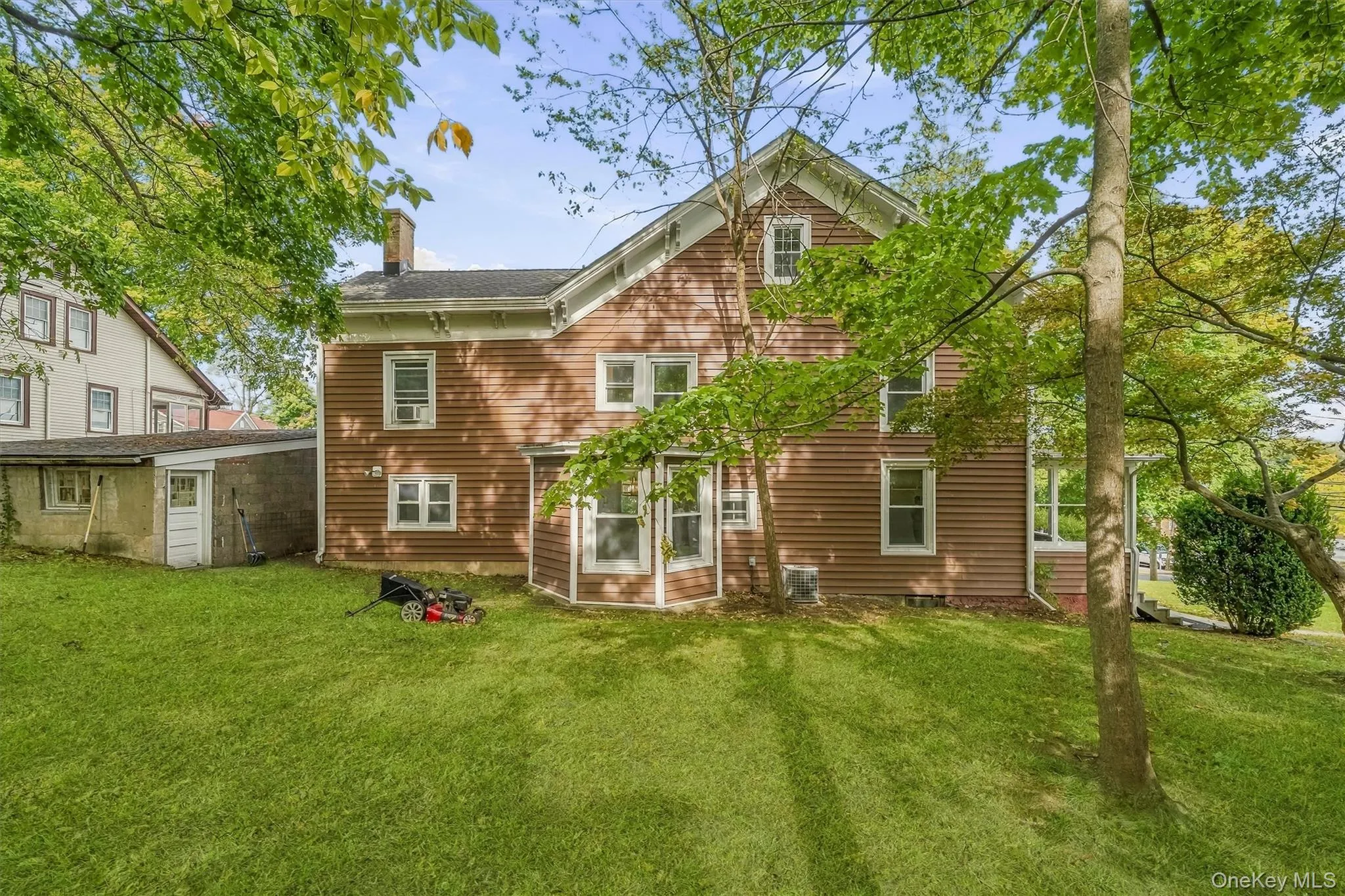 Expansive green lawn with mature trees and a brown-sided residence featuring multiple windows and a chimney Expansive green lawn with mature trees and a brown-sided residence featuring multiple windows and a chimney