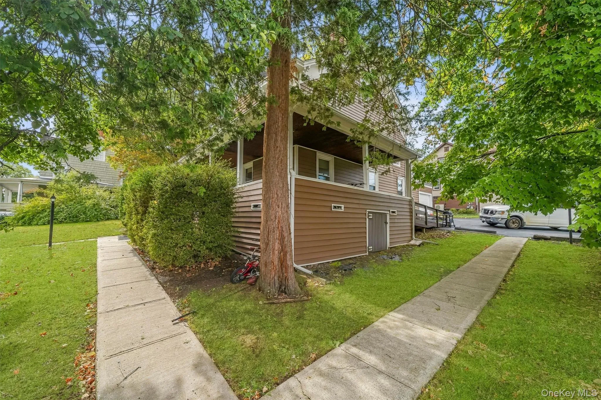 Siding exterior with a covered porch, mature trees, concrete walkways, and a ramp access point Siding exterior with a covered porch, mature trees, concrete walkways, and a ramp access point