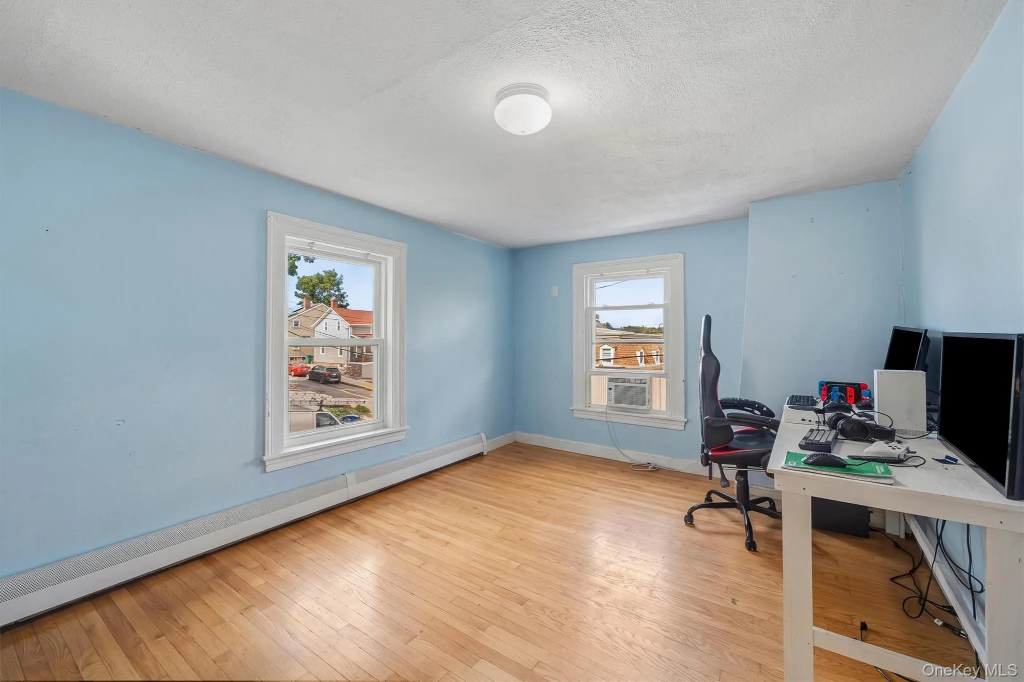 Hardwood flooring, two windows with white trim, light blue painted walls, and a ceiling-mounted light fixture Hardwood flooring, two windows with white trim, light blue painted walls, and a ceiling-mounted light fixture