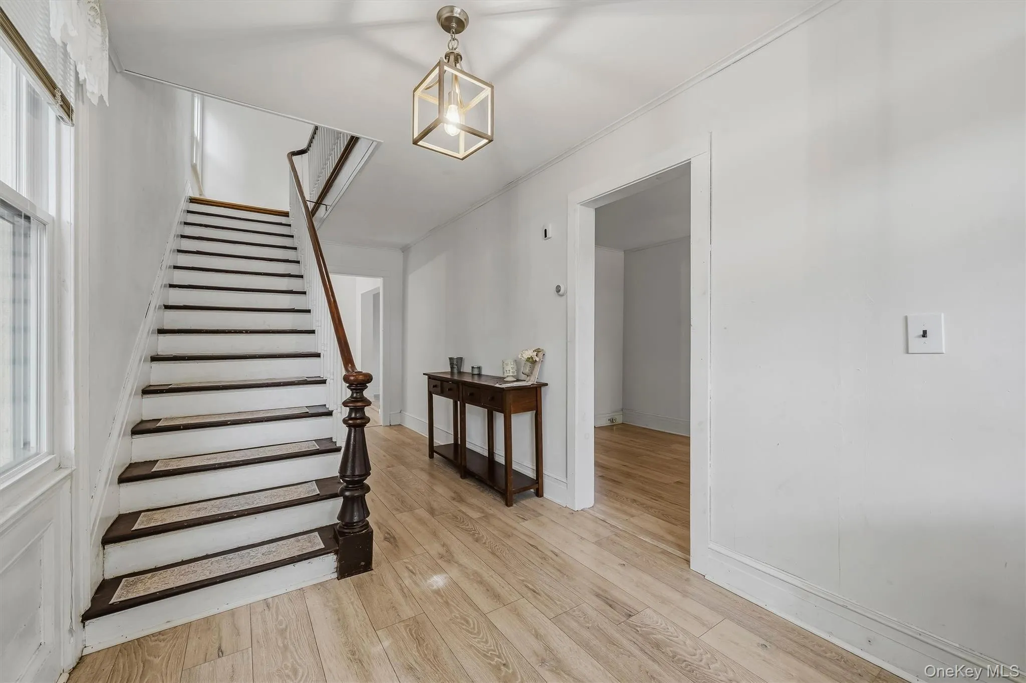 Wood-finish flooring, staircase with dark wood-finish treads and white risers, square caged light fixture, and white wall finishes Wood-finish flooring, staircase with dark wood-finish treads and white risers, square caged light fixture, and white wall finishes