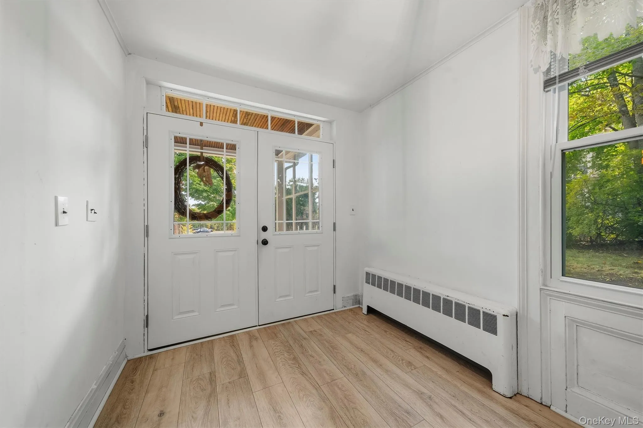Wood-finish flooring, white walls, and a front entry with glass paneled doors Wood-finish flooring, white walls, and a front entry with glass paneled doors