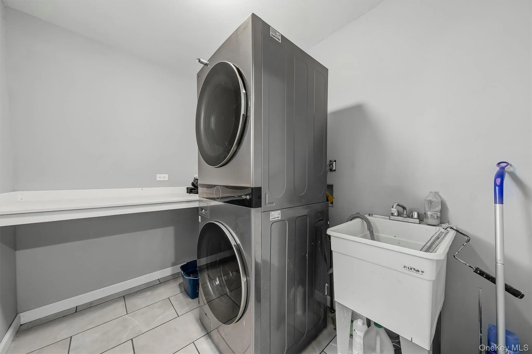 Laundry area featuring a stacked washer and dryer, utility sink with faucet, and light-toned tile flooring Laundry area featuring a stacked washer and dryer, utility sink with faucet, and light-toned tile flooring