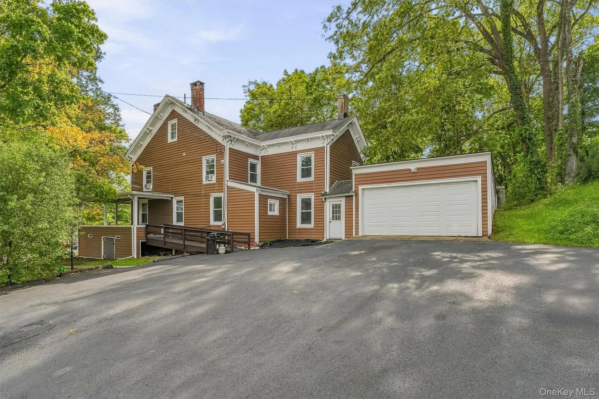 Brown siding exterior with white trim, attached garage with white door, paved driveway, covered porch, and accessible ramp entry Brown siding exterior with white trim, attached garage with white door, paved driveway, covered porch, and accessible ramp entry
