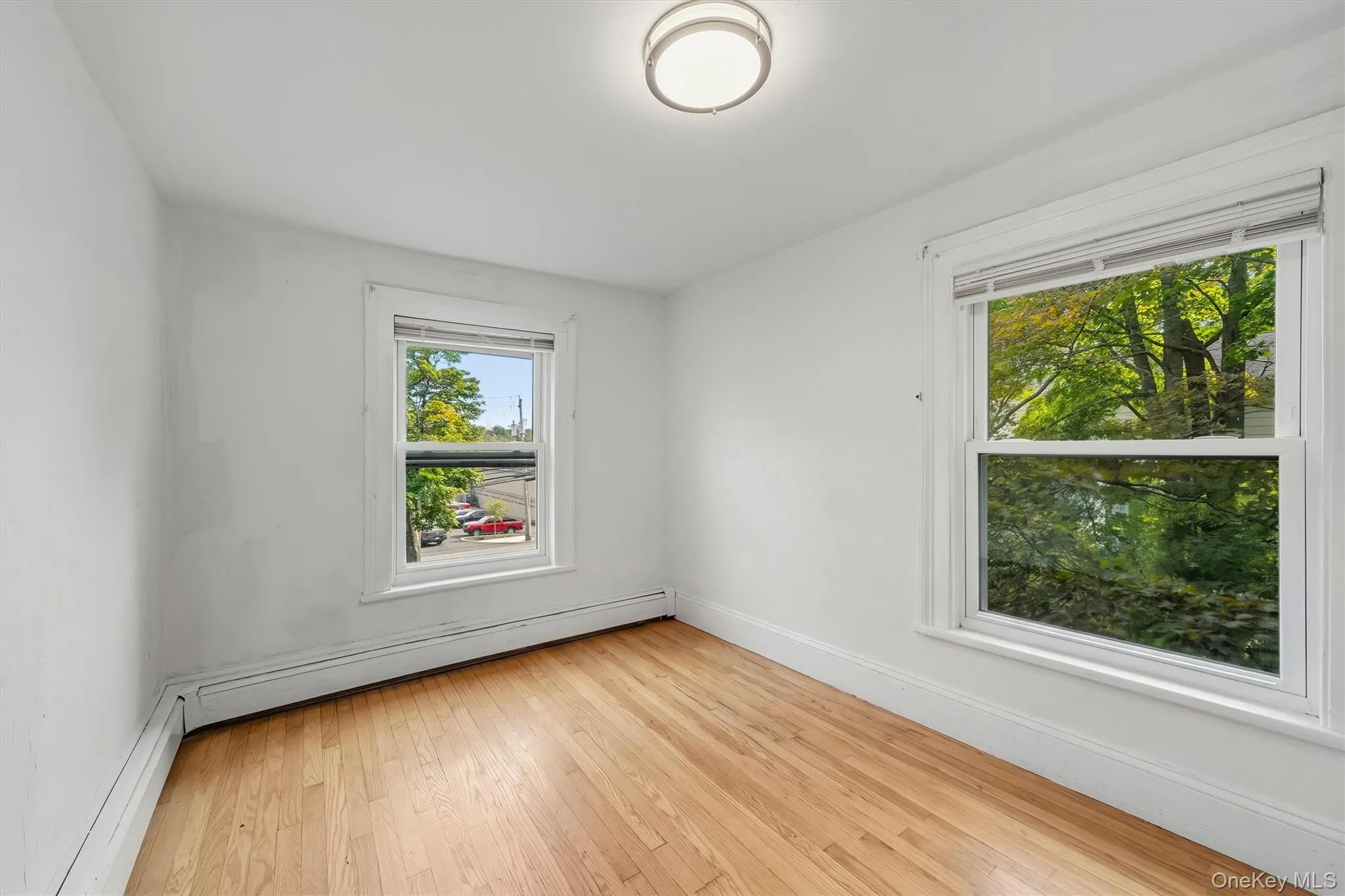 Hardwood flooring, two windows, ceiling-mounted light fixture, white walls, and white trim Hardwood flooring, two windows, ceiling-mounted light fixture, white walls, and white trim