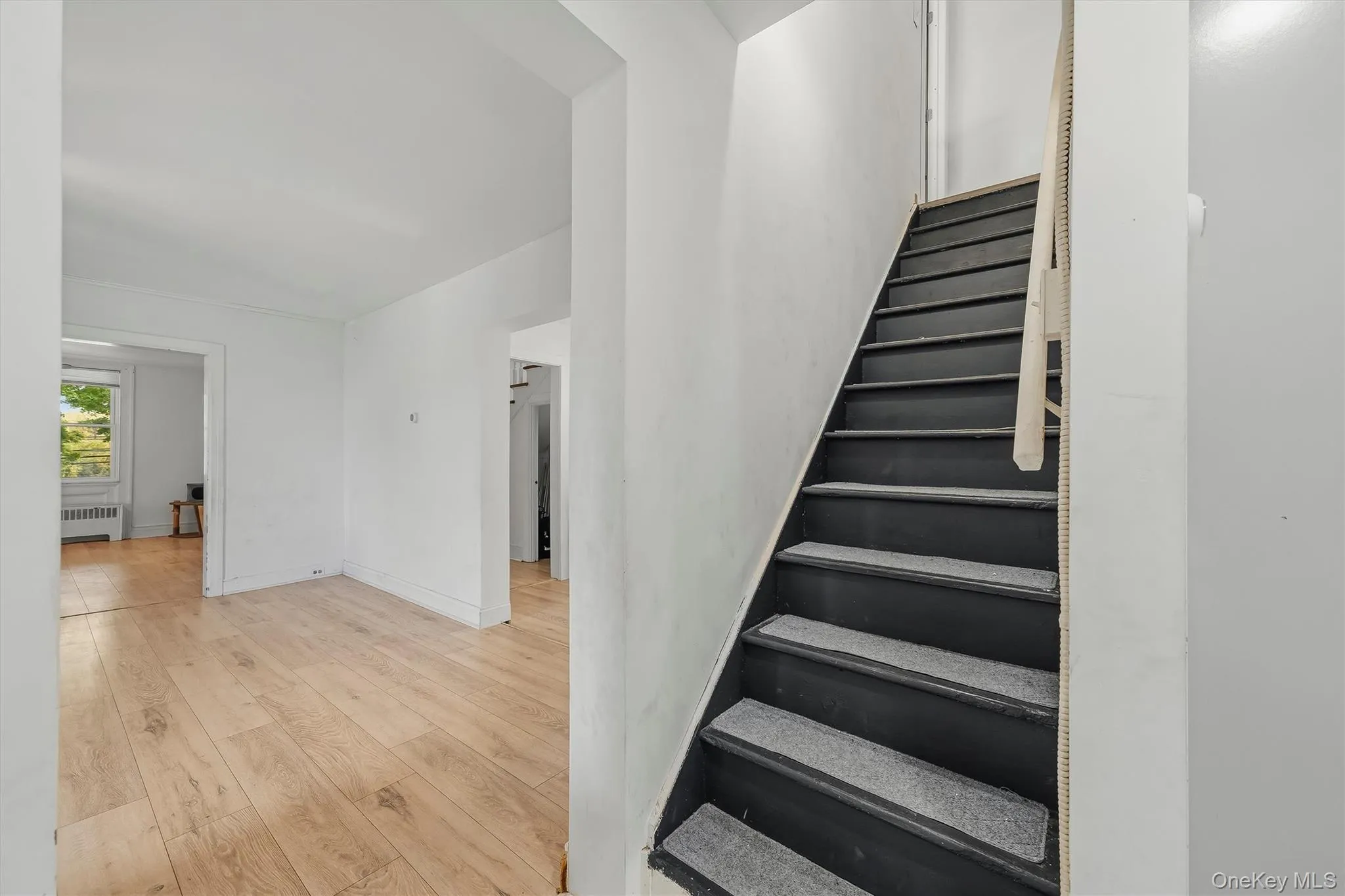 Wood-finish flooring, white wall finishes, dark-painted staircase with textured treads, and multiple doorways Wood-finish flooring, white wall finishes, dark-painted staircase with textured treads, and multiple doorways