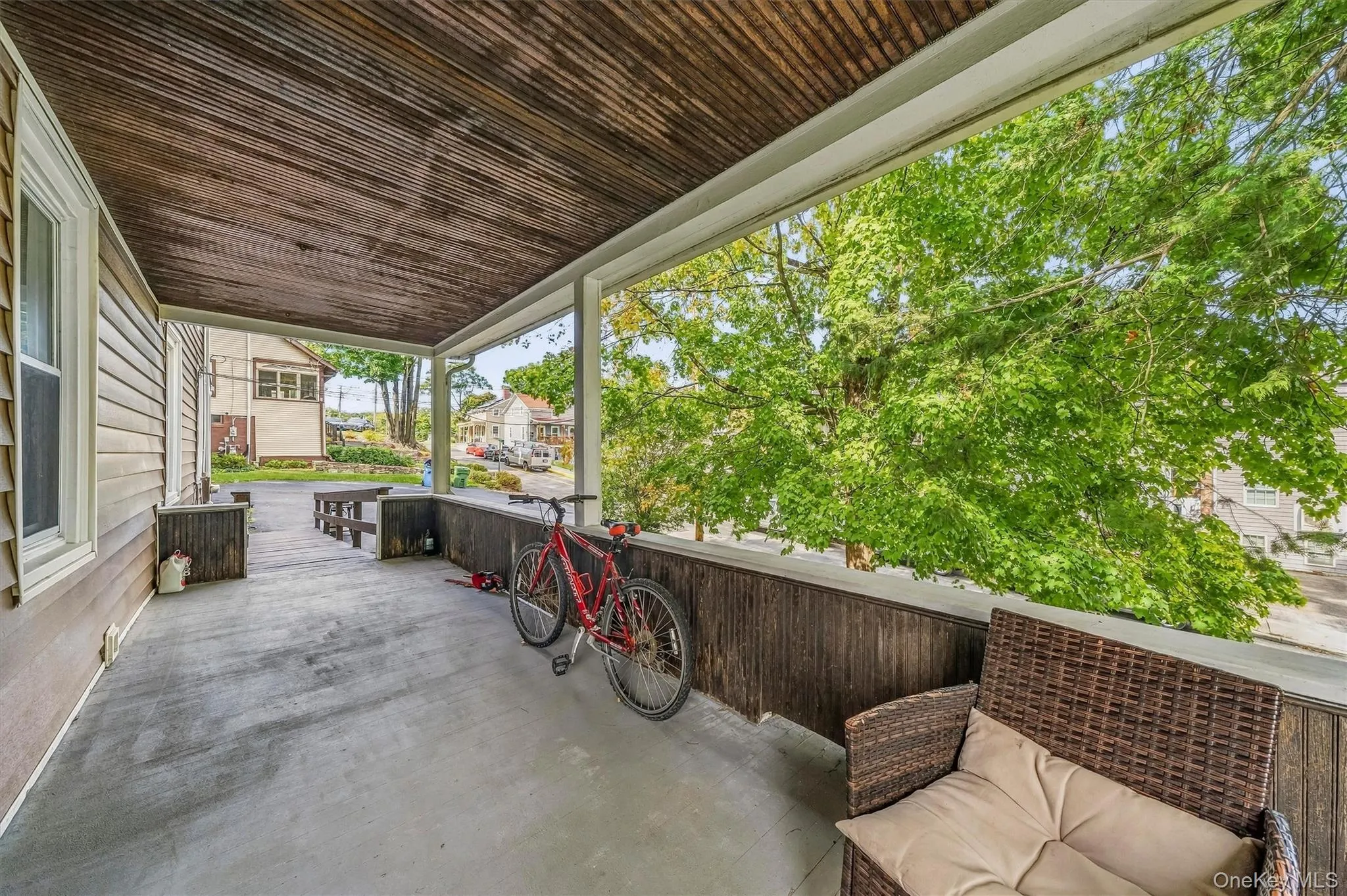 Covered porch featuring a wood-plank ceiling, concrete flooring, and slatted wood railing Covered porch featuring a wood-plank ceiling, concrete flooring, and slatted wood railing
