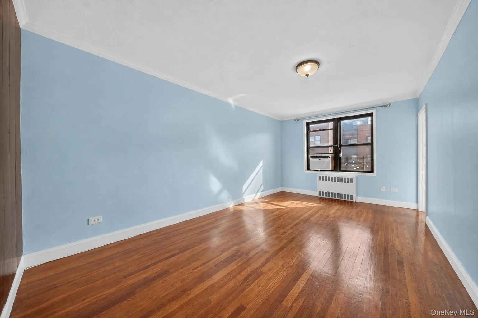 Wood-finish flooring, cased window, wall-mounted air conditioning unit, and flush-mount ceiling light Wood-finish flooring, cased window, wall-mounted air conditioning unit, and flush-mount ceiling light