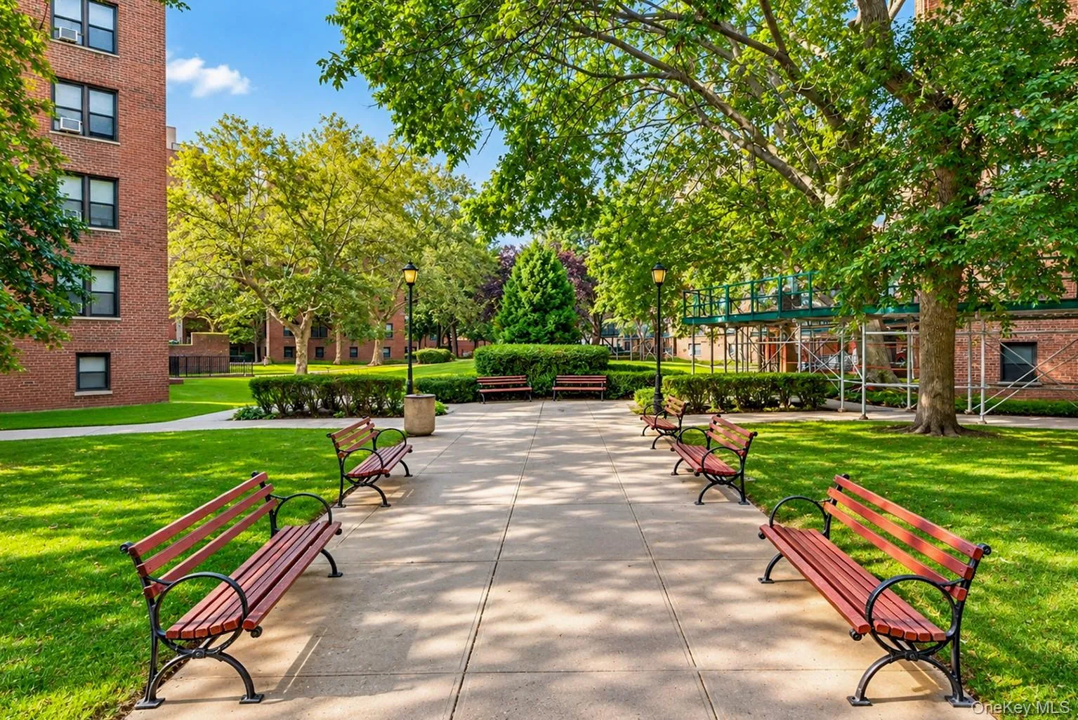 Expansive common grounds featuring a concrete pathway, manicured lawns, mature trees, and multiple park benches Expansive common grounds featuring a concrete pathway, manicured lawns, mature trees, and multiple park benches