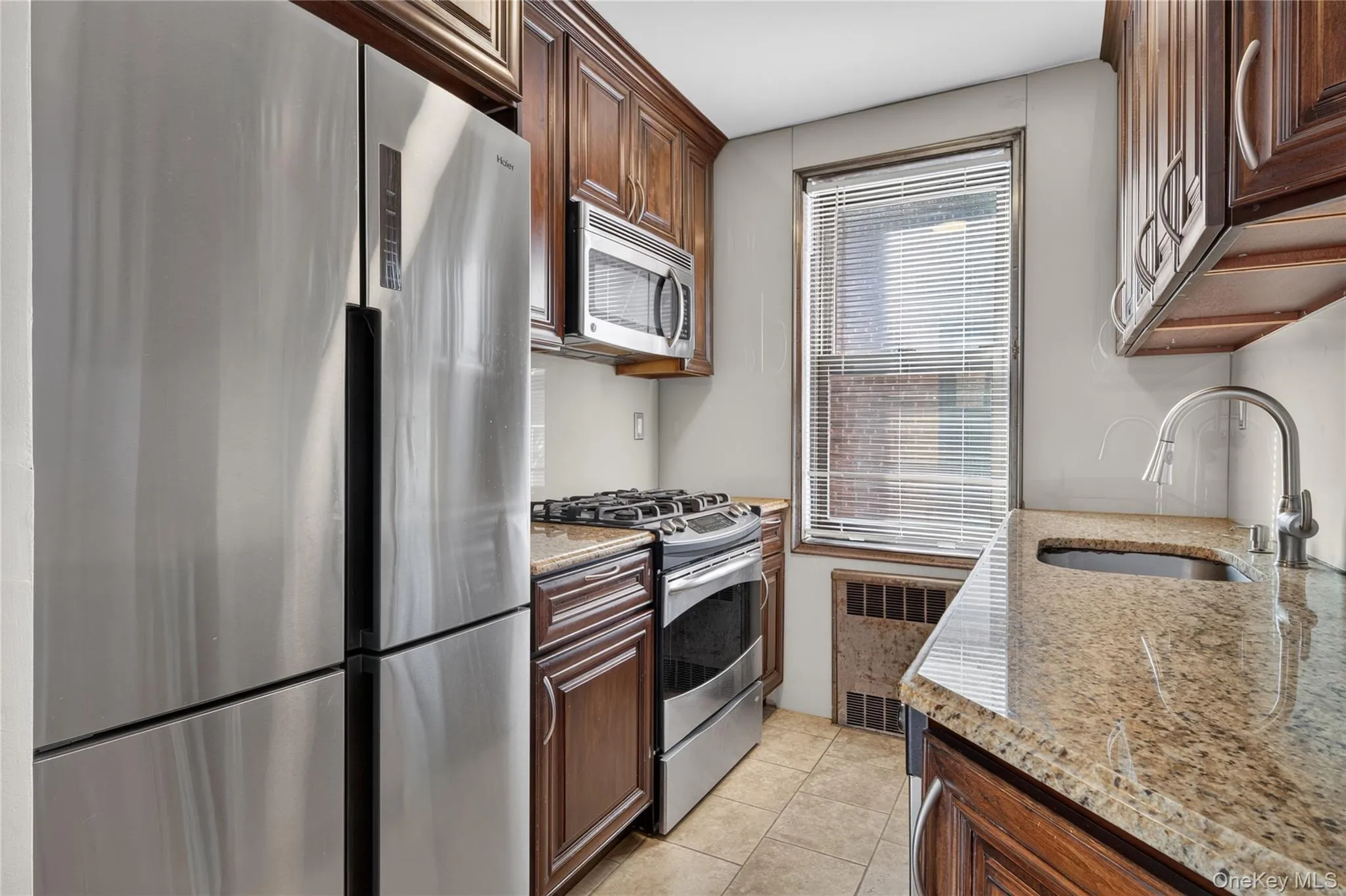 Kitchen featuring rich wood cabinetry, stone countertops, stainless steel appliances, and a window with blinds Kitchen featuring rich wood cabinetry, stone countertops, stainless steel appliances, and a window with blinds