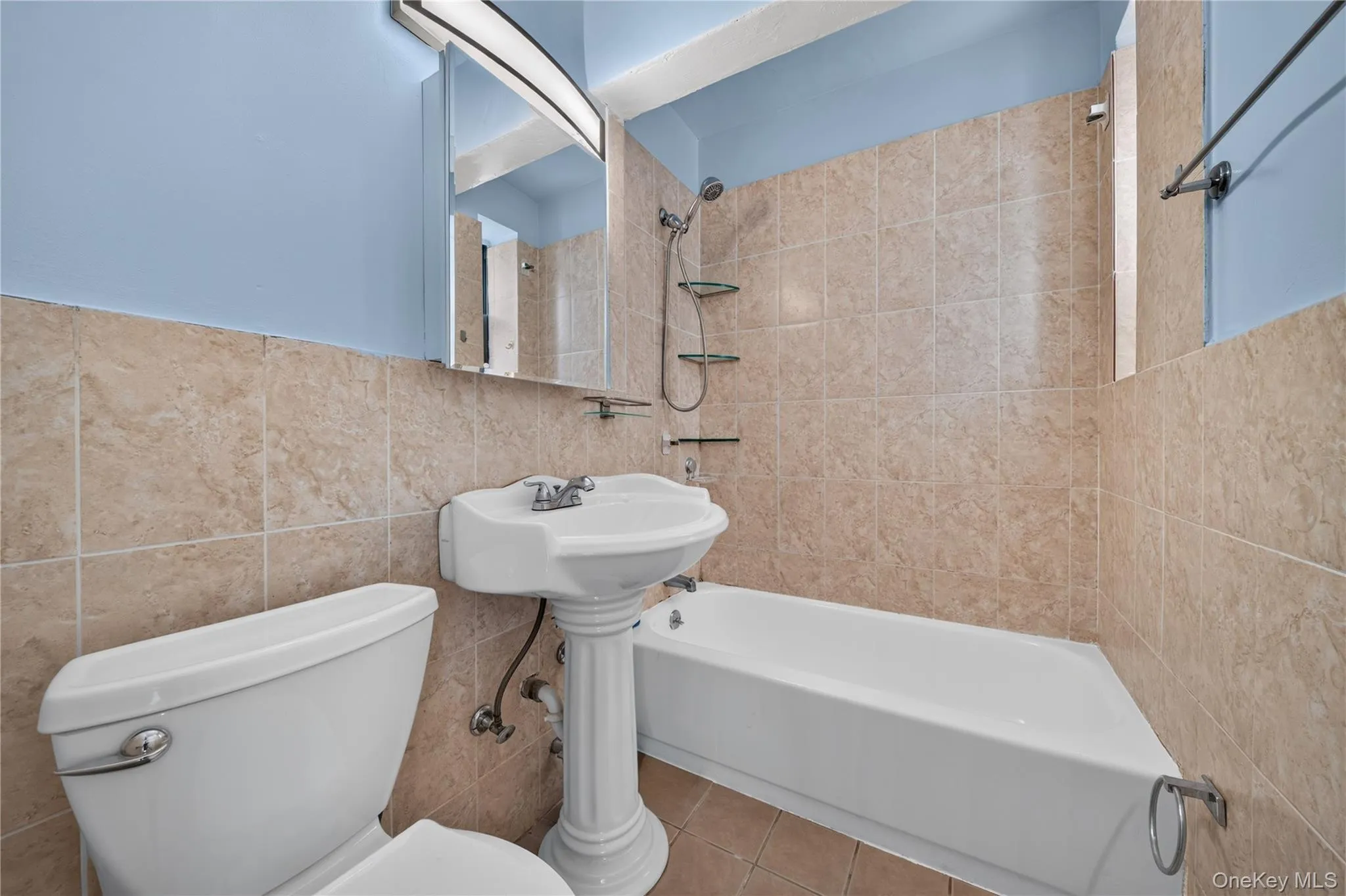 Bathroom featuring floor-to-ceiling tiling, pedestal sink, shower-tub combination, and wall-mounted medicine cabinet with integrated lighting Bathroom featuring floor-to-ceiling tiling, pedestal sink, shower-tub combination, and wall-mounted medicine cabinet with integrated lighting