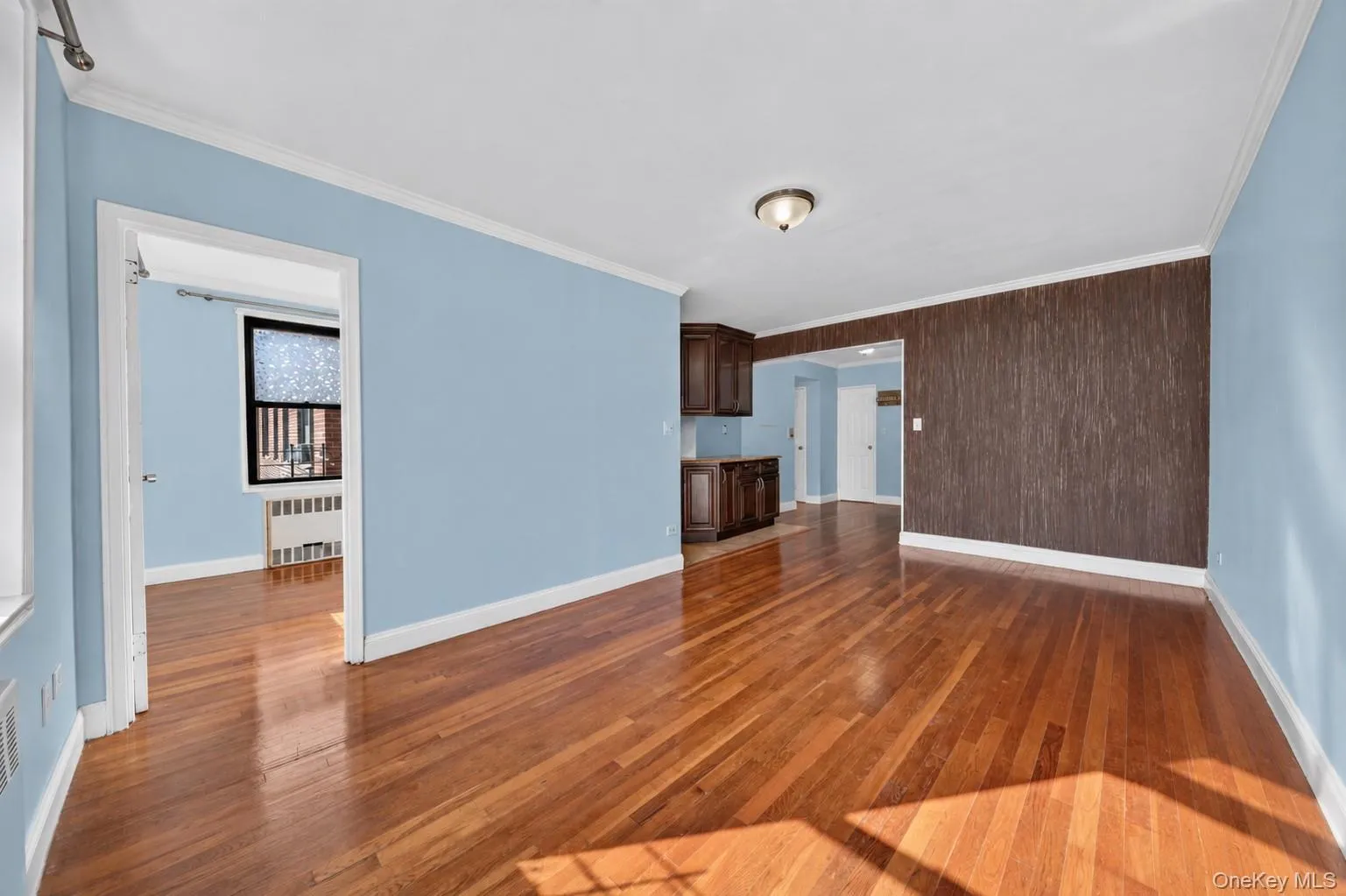 Hardwood flooring, crown molding, built-in cabinetry, ceiling-mounted light fixture, and a window with a radiator Hardwood flooring, crown molding, built-in cabinetry, ceiling-mounted light fixture, and a window with a radiator