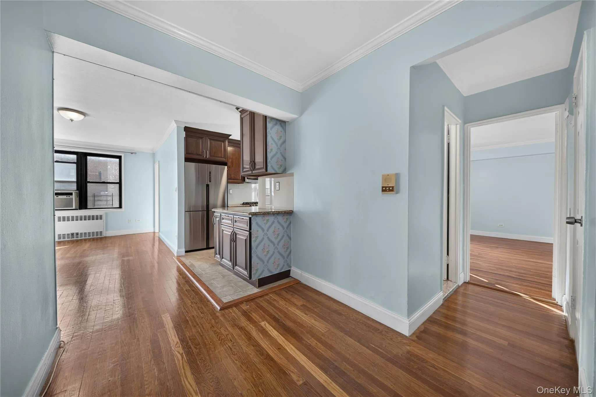 Hardwood flooring, kitchen area with dark wood-finish cabinetry, stainless steel refrigerator, and recessed lighting Hardwood flooring, kitchen area with dark wood-finish cabinetry, stainless steel refrigerator, and recessed lighting