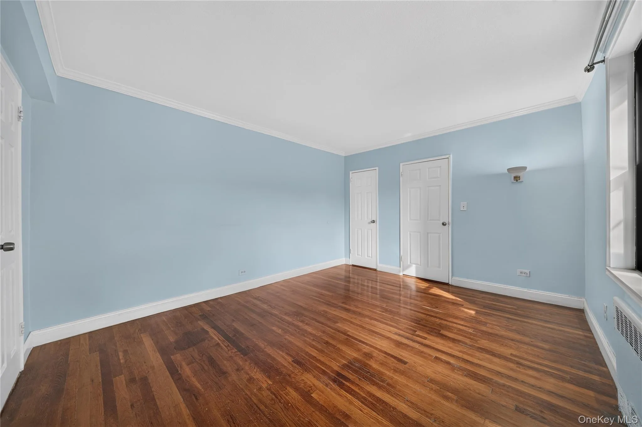 Hardwood flooring, painted walls, white trim, and a window with a radiator below Hardwood flooring, painted walls, white trim, and a window with a radiator below