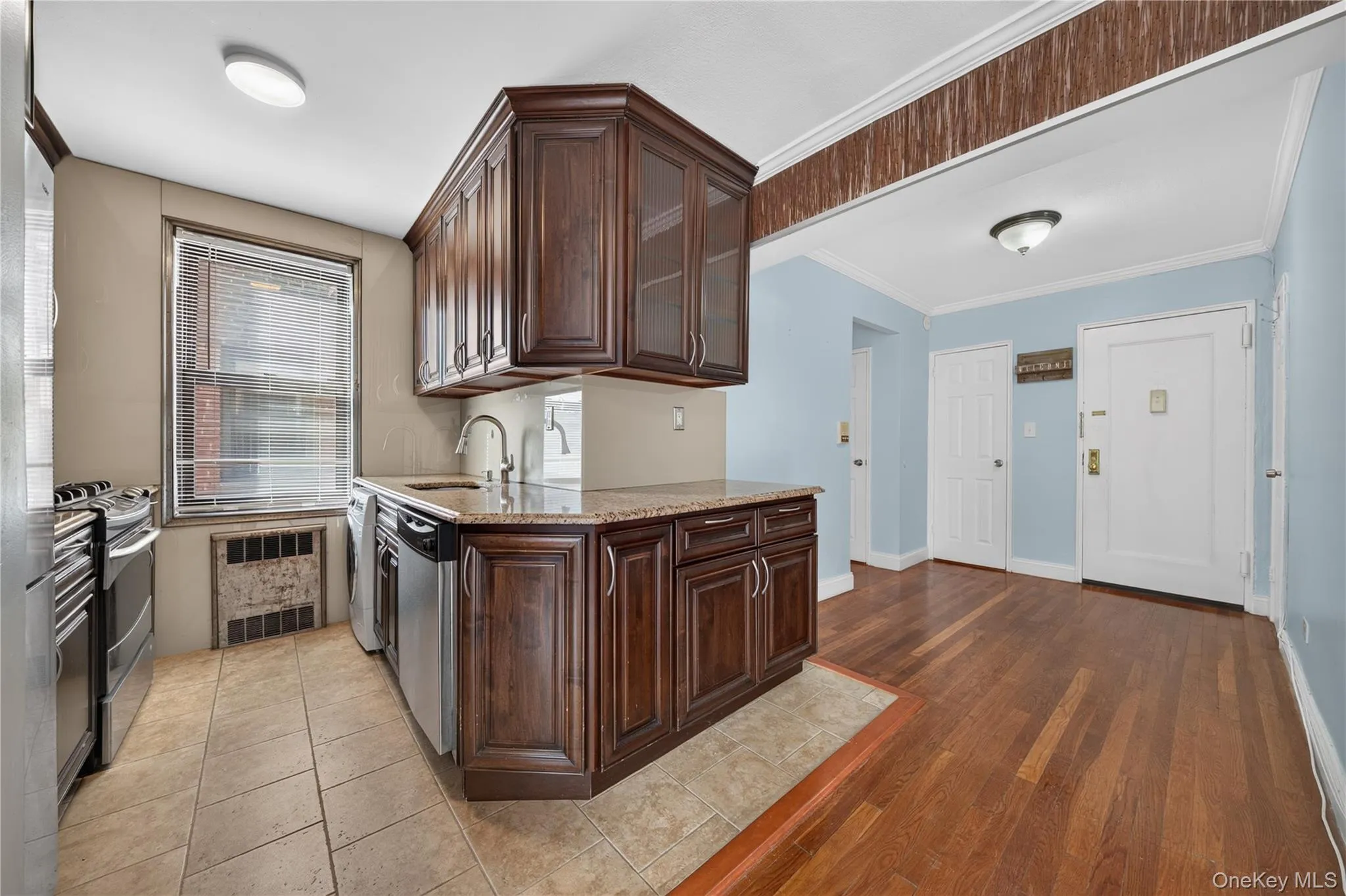 Elegant kitchen and dining area featuring rich wood cabinetry with detailed paneling, stainless steel appliances, and tile flooring Elegant kitchen and dining area featuring rich wood cabinetry with detailed paneling, stainless steel appliances, and tile flooring