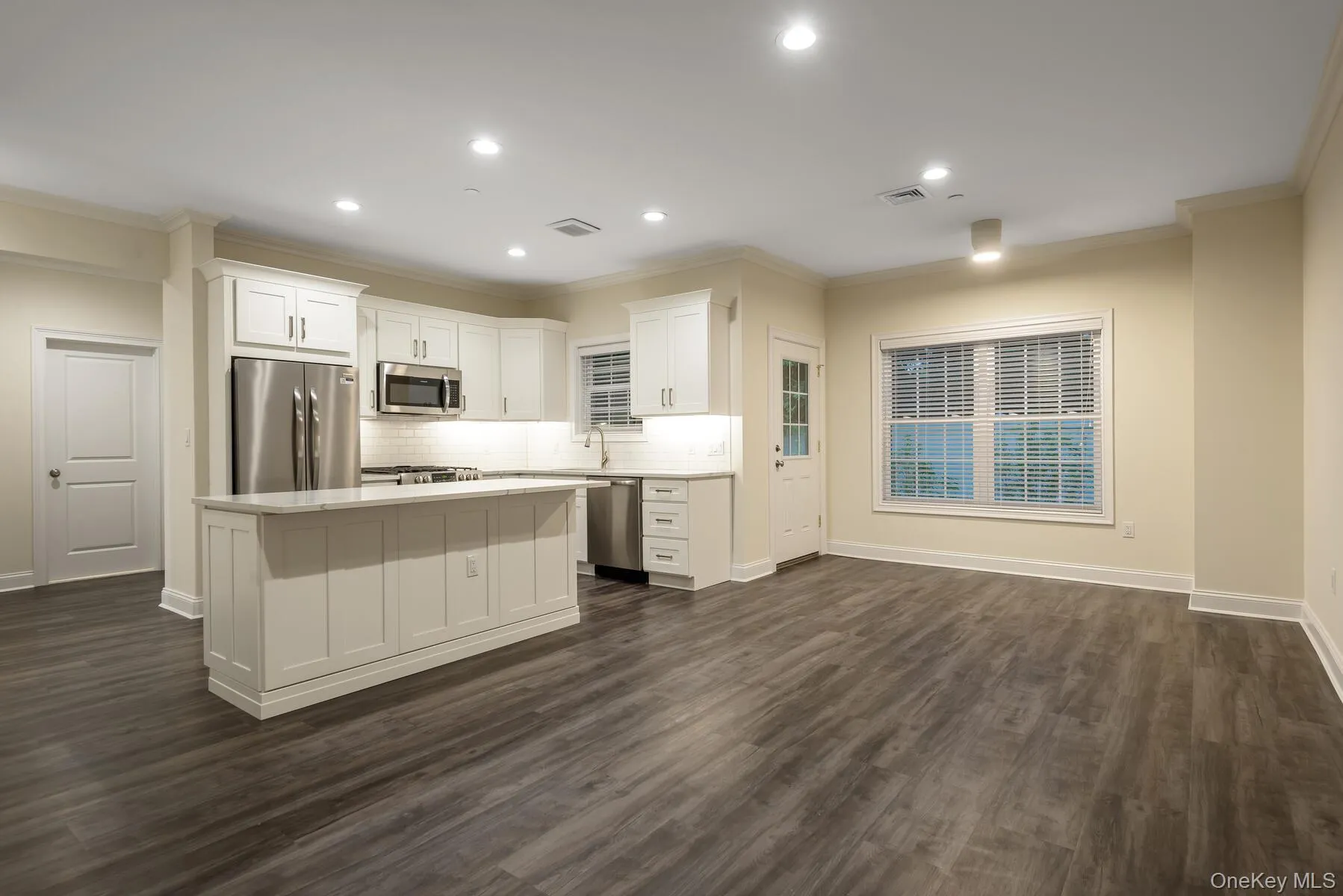 Open-concept living area featuring wood-finish flooring, recessed lighting, and crown molding Open-concept living area featuring wood-finish flooring, recessed lighting, and crown molding