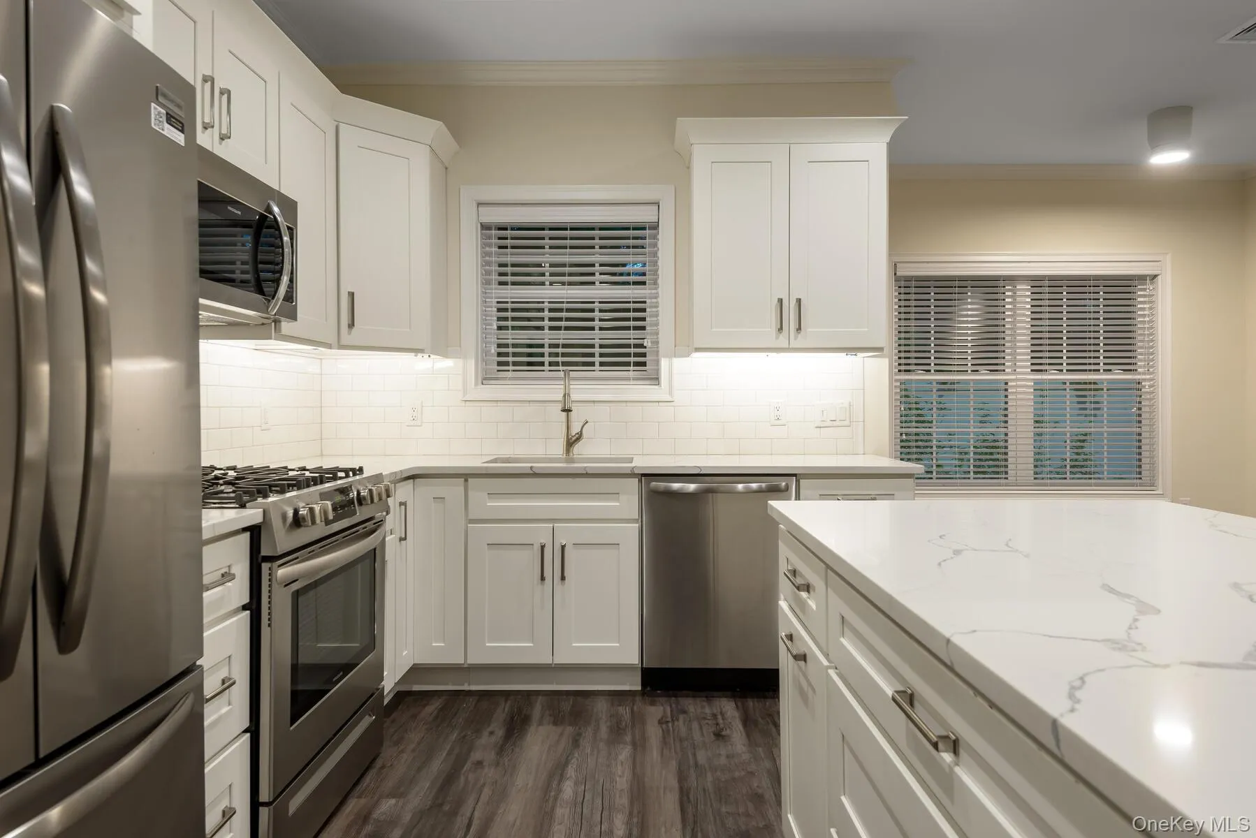 Contemporary kitchen featuring white shaker cabinetry, stainless steel appliances, white subway tile backsplash, and wood-finish flooring Contemporary kitchen featuring white shaker cabinetry, stainless steel appliances, white subway tile backsplash, and wood-finish flooring