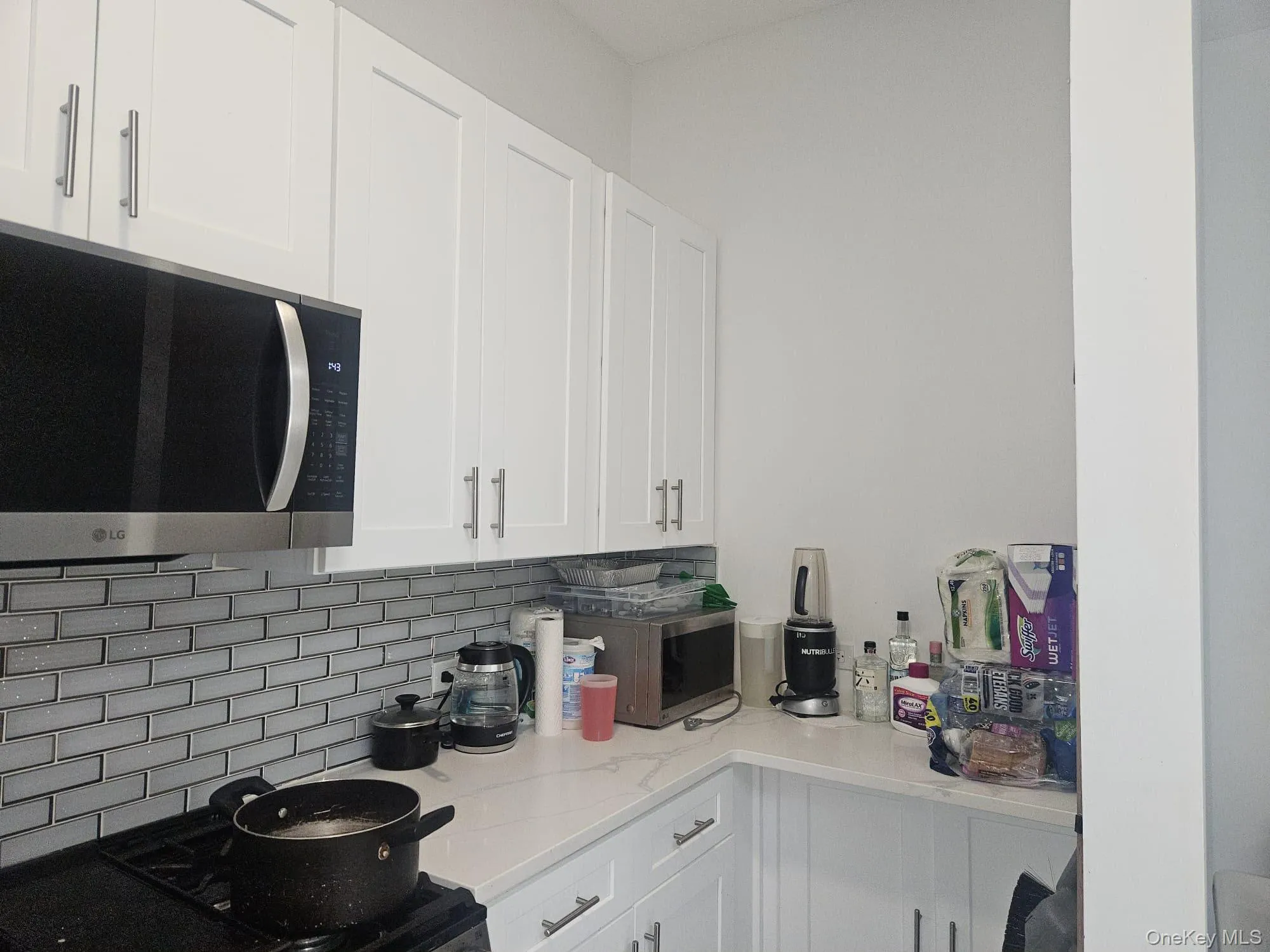 White shaker-style cabinetry, stainless steel microwave, white subway tile backsplash, and light-colored countertops White shaker-style cabinetry, stainless steel microwave, white subway tile backsplash, and light-colored countertops