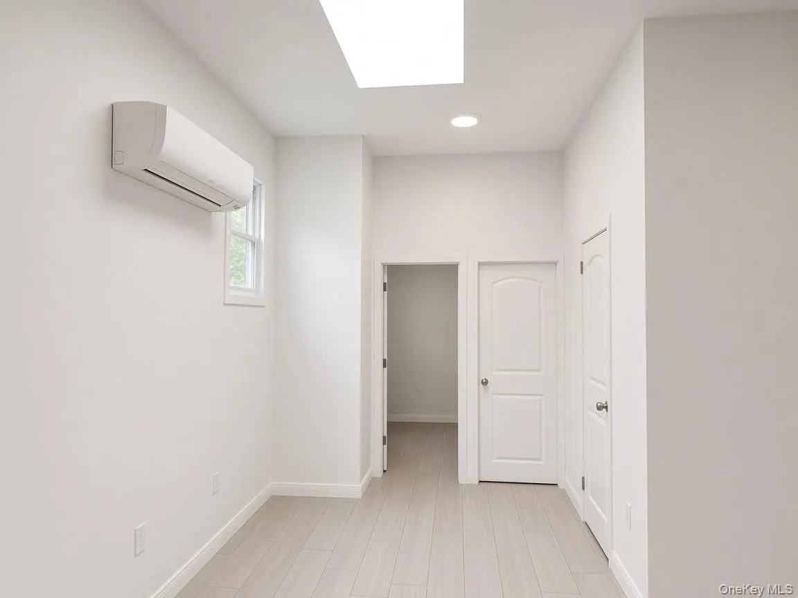 Recessed lighting, skylight, wood-finish flooring, white paneled doors, and a wall-mounted climate control unit Recessed lighting, skylight, wood-finish flooring, white paneled doors, and a wall-mounted climate control unit