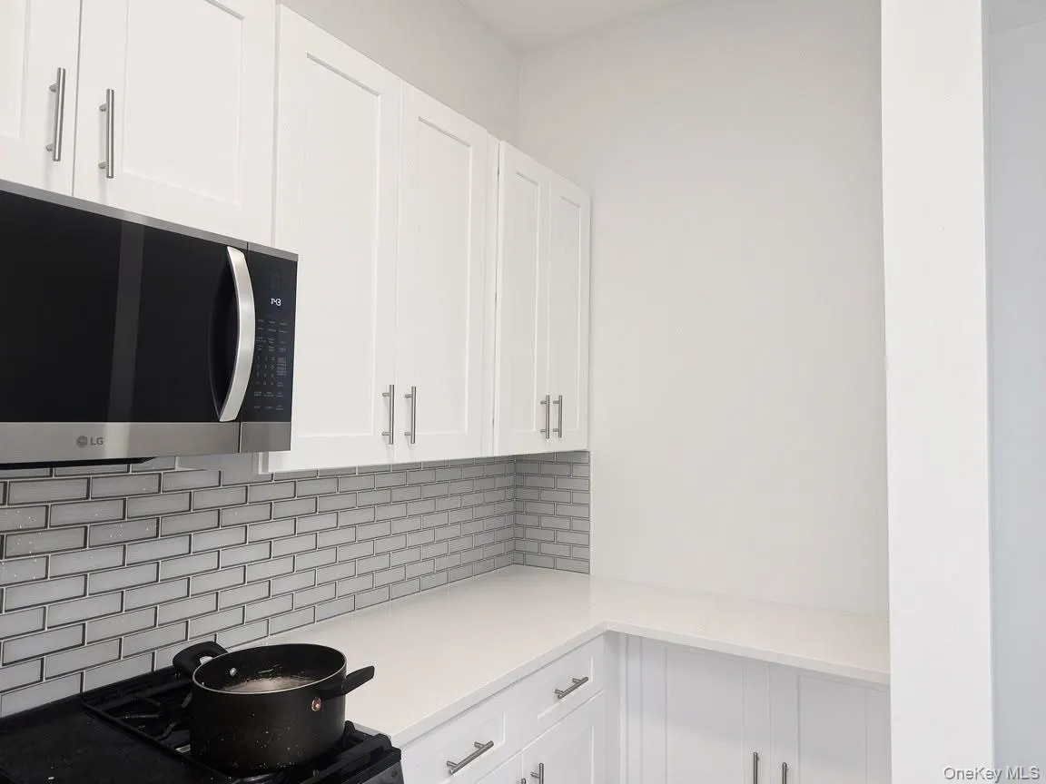White shaker-style cabinetry with brushed nickel hardware, stainless steel over-the-range microwave, white subway tile backsplash, and light-toned countertops White shaker-style cabinetry with brushed nickel hardware, stainless steel over-the-range microwave, white subway tile backsplash, and light-toned countertops