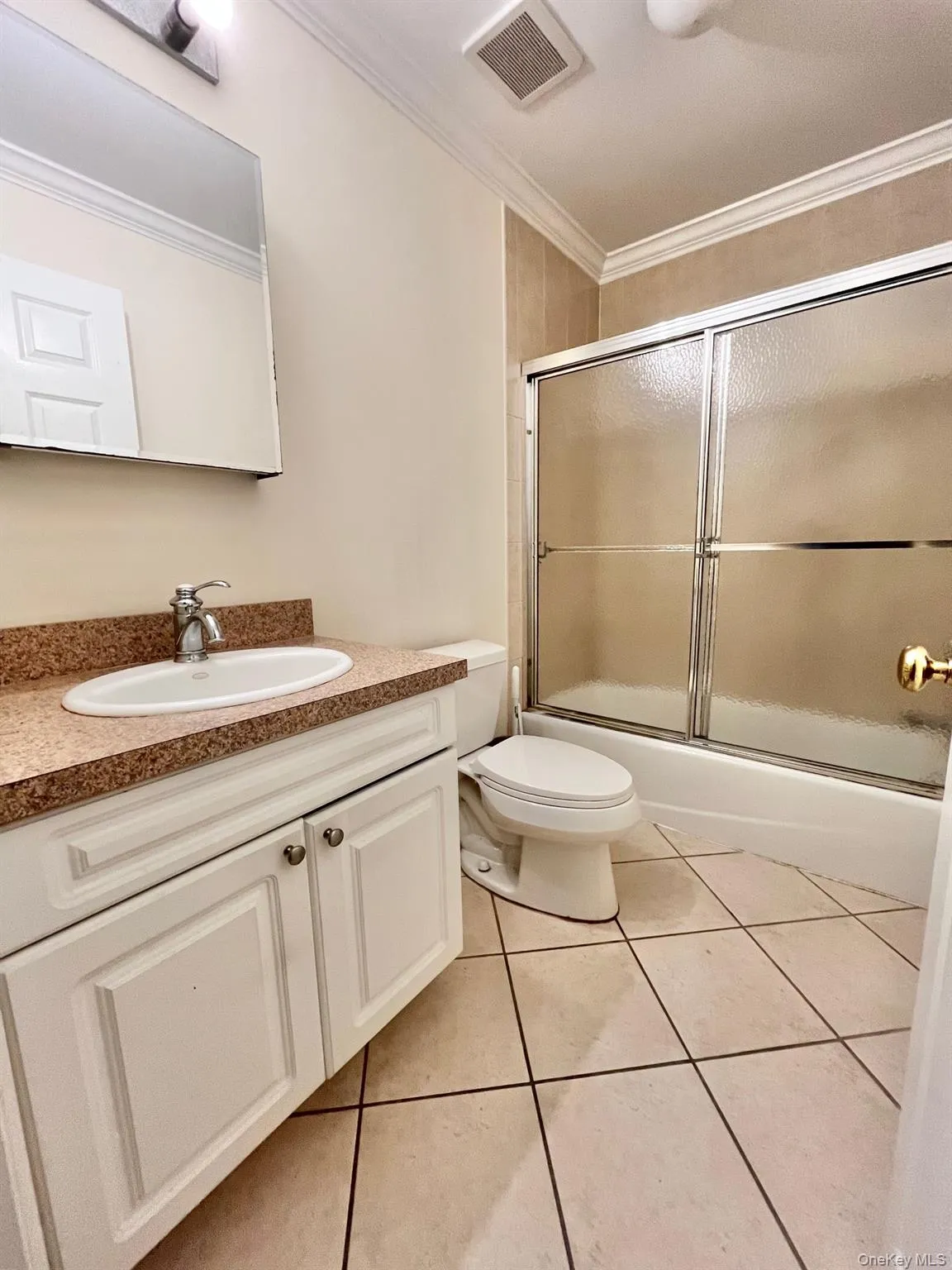 Bathroom featuring vanity, ornamental molding, light tile patterned flooring, and shower / bath combination with glass door Bathroom featuring vanity, ornamental molding, light tile patterned flooring, and shower / bath combination with glass door