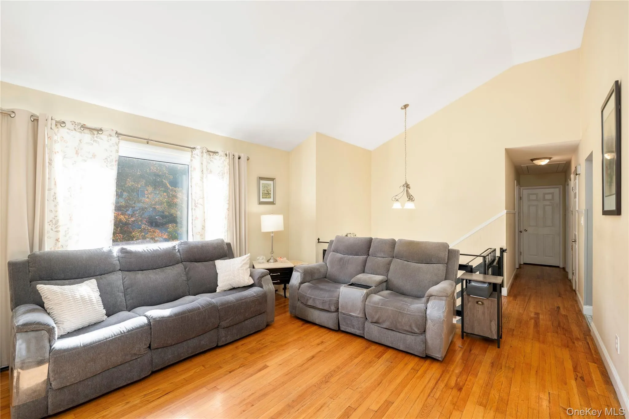 Vaulted ceiling, wood-finish flooring, large window, two-panel interior door, and pendant lighting fixture Vaulted ceiling, wood-finish flooring, large window, two-panel interior door, and pendant lighting fixture