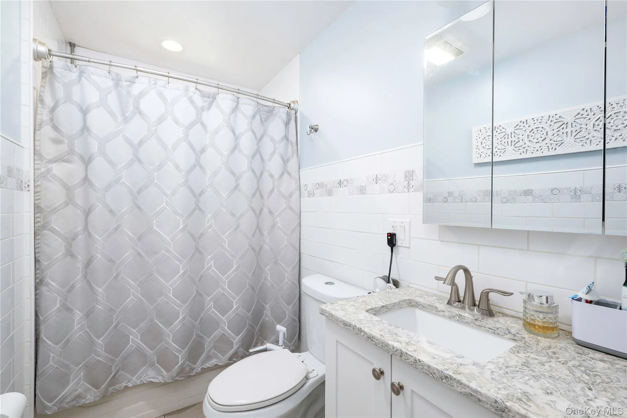 Bathroom featuring a single vanity with a light-toned countertop, white cabinetry, a rectangular undermount sink, and a mirrored medicine cabinet Bathroom featuring a single vanity with a light-toned countertop, white cabinetry, a rectangular undermount sink, and a mirrored medicine cabinet