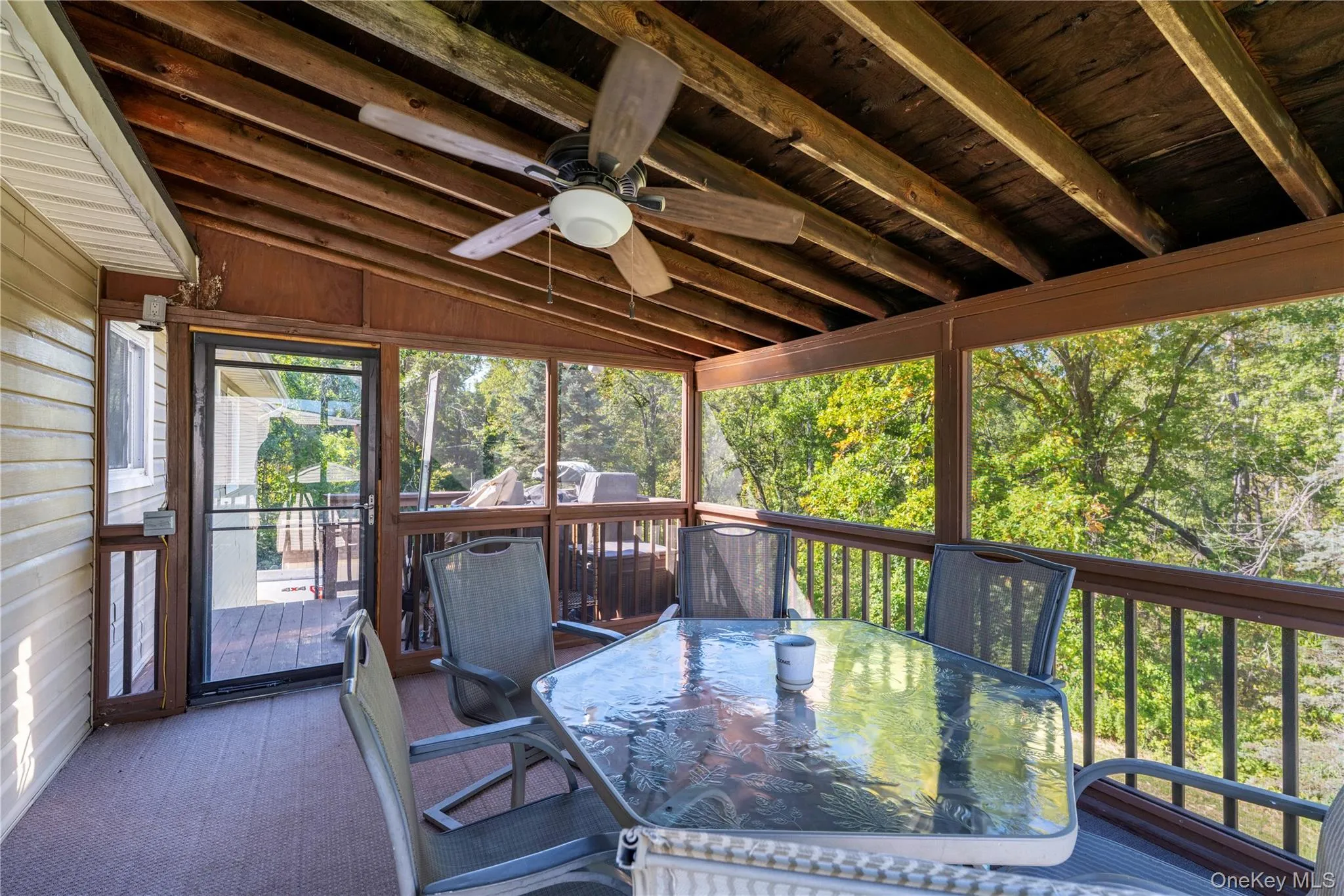 Screened-in deck featuring a wood-finish ceiling with exposed beams, ceiling fan, and a light wood-finish railing system Screened-in deck featuring a wood-finish ceiling with exposed beams, ceiling fan, and a light wood-finish railing system