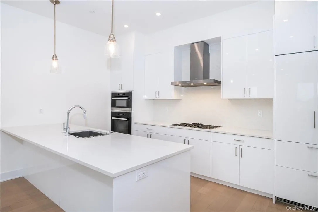 Kitchen featuring white gas stovetop, white cabinets, wall chimney exhaust hood, sink, and pendant lighting Kitchen featuring white gas stovetop, white cabinets, wall chimney exhaust hood, sink, and pendant lighting