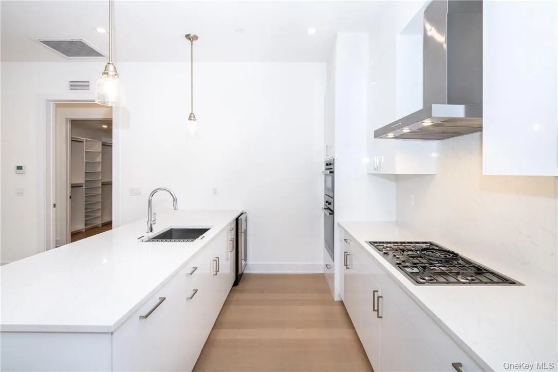Kitchen featuring stainless steel appliances, wall chimney range hood, decorative light fixtures, white cabinets, and light hardwood / wood-style flooring Kitchen featuring stainless steel appliances, wall chimney range hood, decorative light fixtures, white cabinets, and light hardwood / wood-style flooring