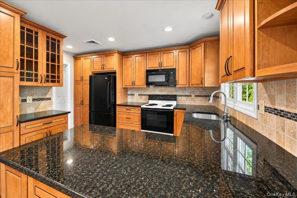 A stylish blend of dark stone countertops, light wood-finish cabinetry, and sleek black built-in appliances creates a modern, inviting kitchen, complemented by a tile backsplash and stainless steel sink with a high-arch faucet. A stylish blend of dark stone countertops, light wood-finish cabinetry, and sleek black built-in appliances creates a modern, inviting kitchen, complemented by a tile backsplash and stainless steel sink with a high-arch faucet.