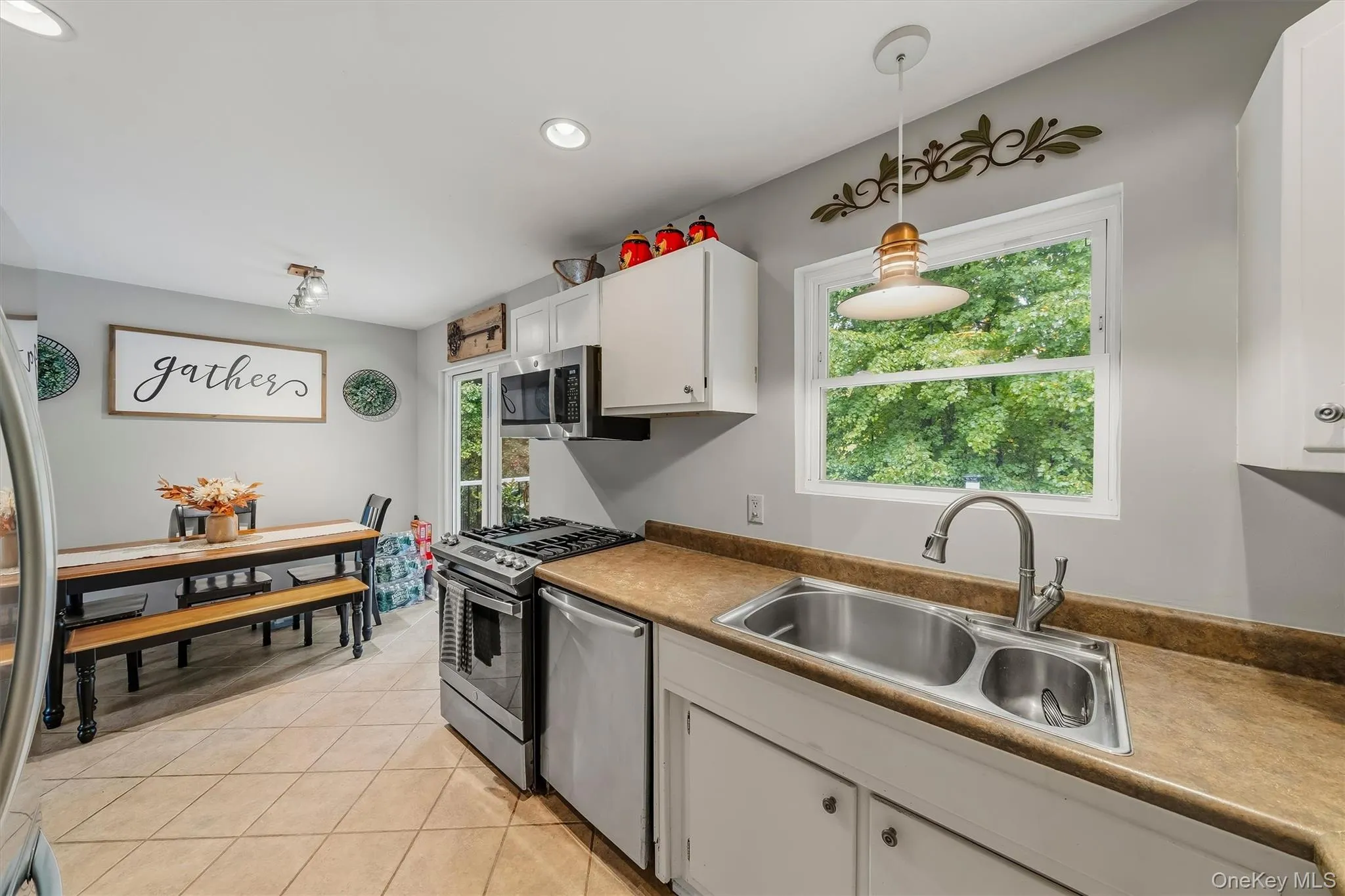 Kitchen featuring tile flooring, stainless steel appliances, white cabinetry, and a double-basin sink Kitchen featuring tile flooring, stainless steel appliances, white cabinetry, and a double-basin sink