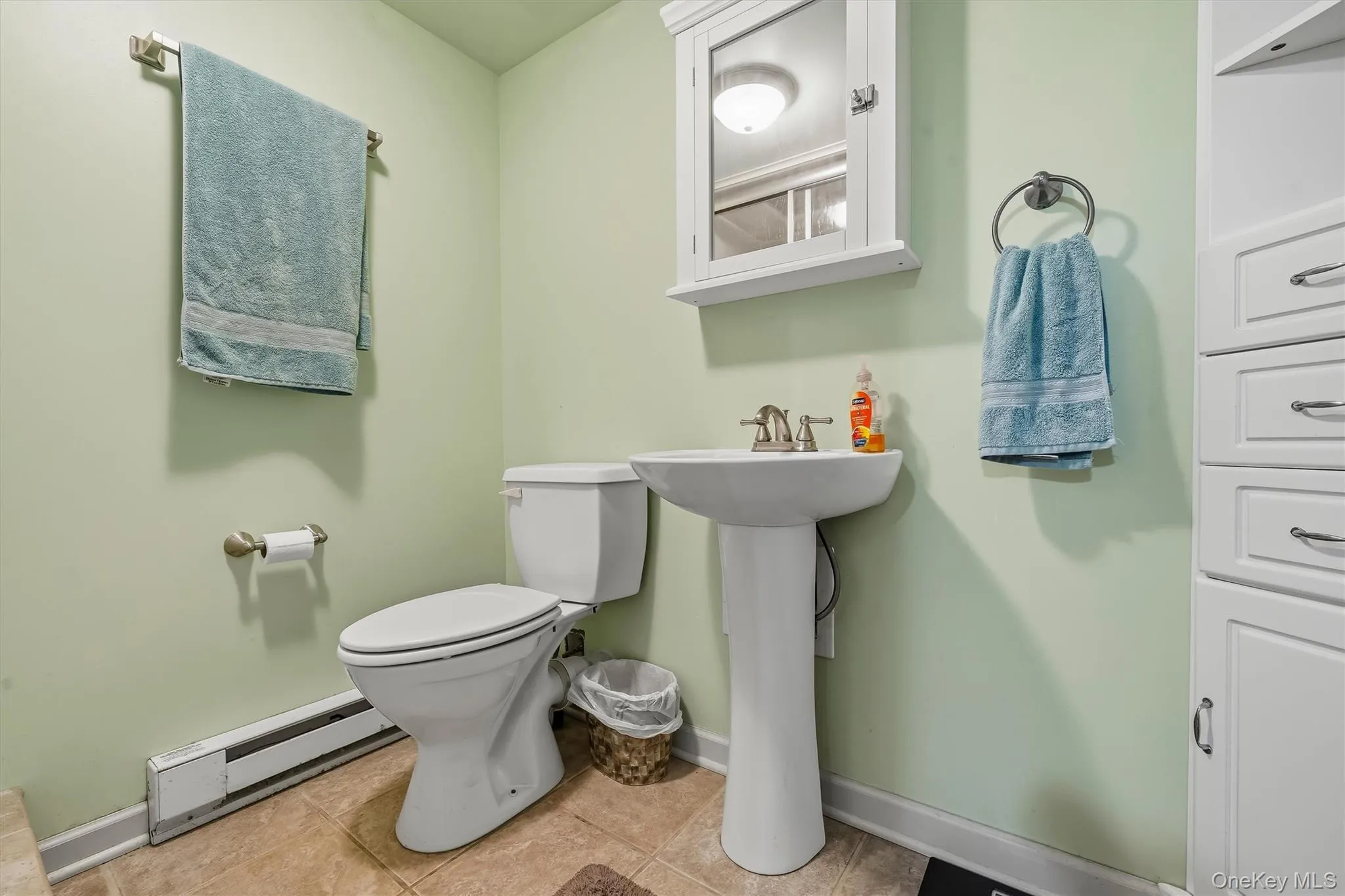 Pedestal sink, wall-mounted medicine cabinet with mirror, built-in white cabinetry, light green wall finish, and tiled flooring Pedestal sink, wall-mounted medicine cabinet with mirror, built-in white cabinetry, light green wall finish, and tiled flooring