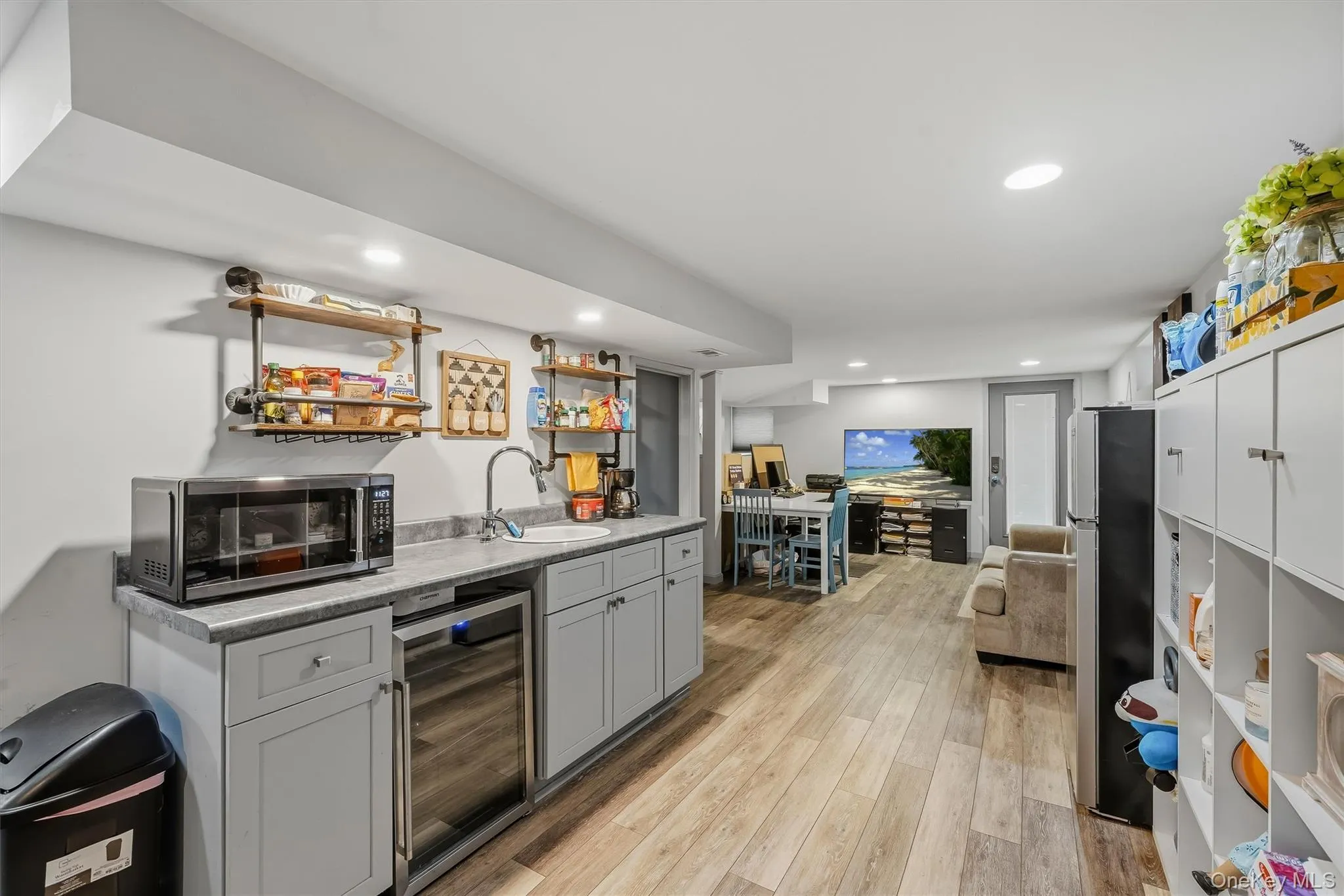 Wood-finish flooring throughout, kitchenette with gray cabinetry and stone-look countertop, recessed lighting, and wall-mounted shelving Wood-finish flooring throughout, kitchenette with gray cabinetry and stone-look countertop, recessed lighting, and wall-mounted shelving