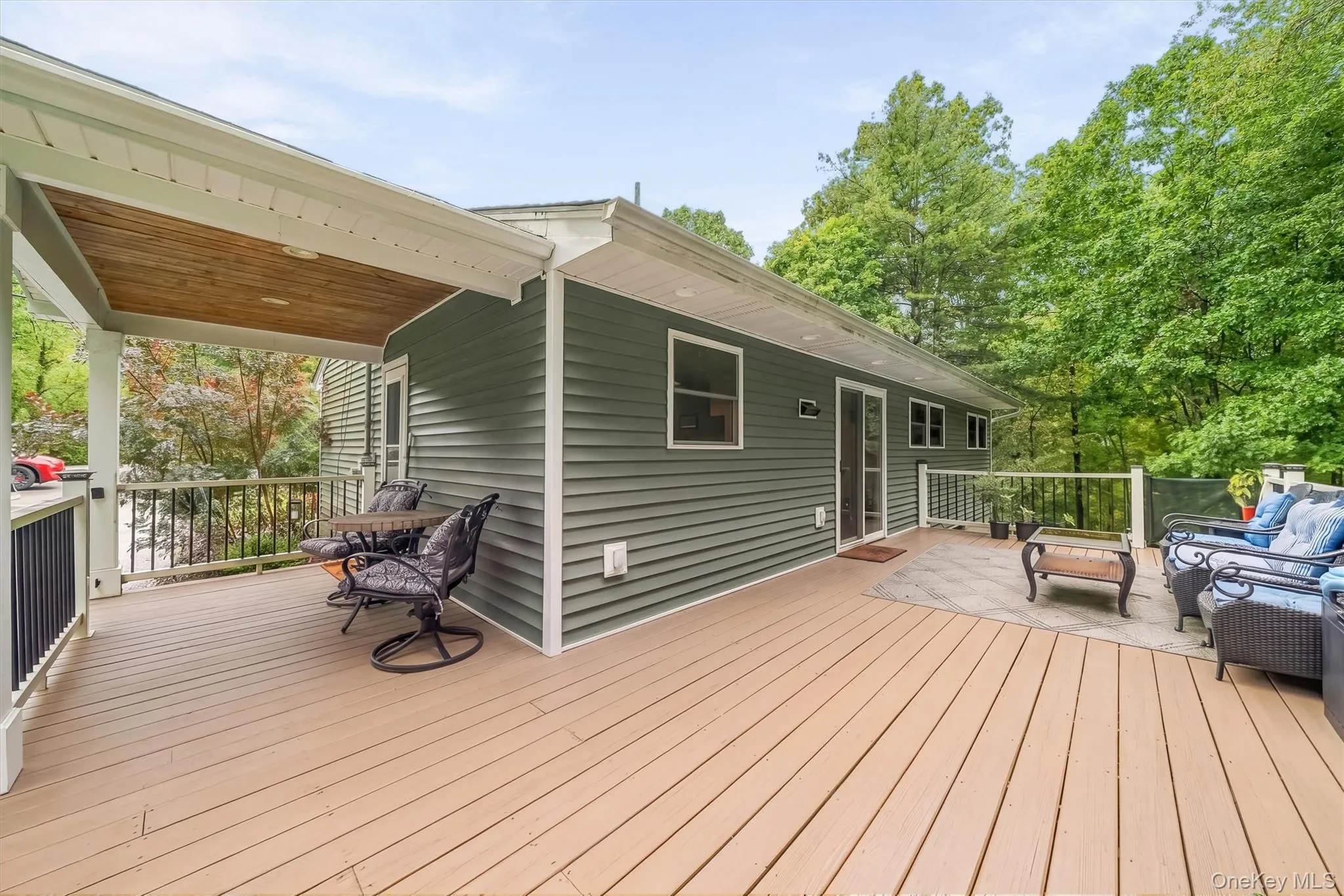 Expansive wood-finish deck with a partial covered area featuring a wood-panel ceiling, solid green siding, and multiple windows Expansive wood-finish deck with a partial covered area featuring a wood-panel ceiling, solid green siding, and multiple windows