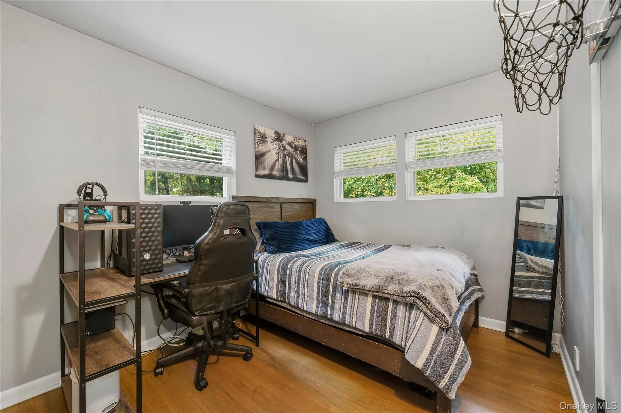 Hardwood-finish flooring, three windows with blinds, gray wall paint, and a wood-finish headboard Hardwood-finish flooring, three windows with blinds, gray wall paint, and a wood-finish headboard