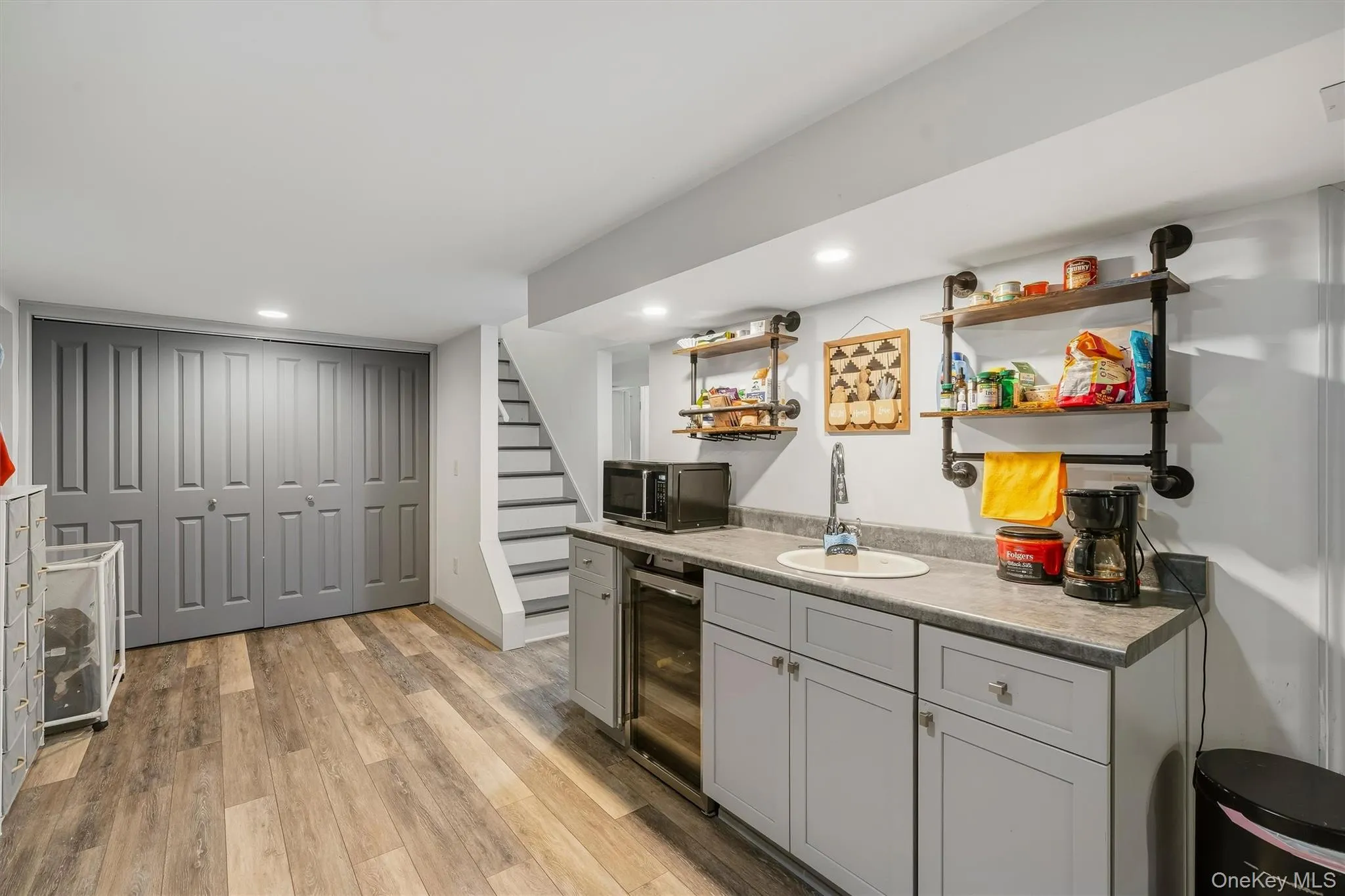 Wood-finish flooring, built-in cabinetry, under-counter beverage cooler, recessed lighting, and open industrial-style shelving Wood-finish flooring, built-in cabinetry, under-counter beverage cooler, recessed lighting, and open industrial-style shelving