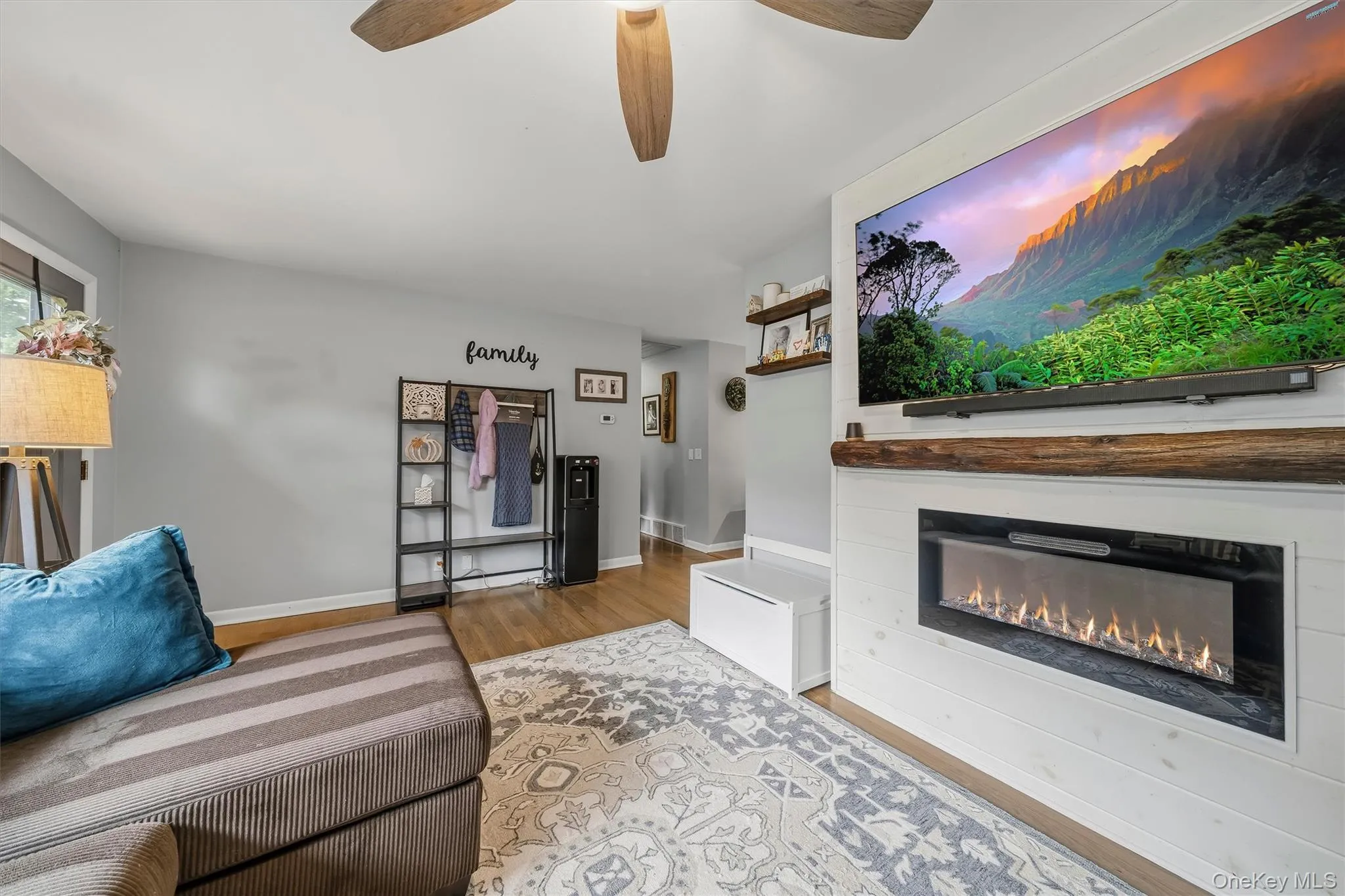 Wood-finish flooring, ceiling fan, built-in electric fireplace with a wood mantel, and floating shelves Wood-finish flooring, ceiling fan, built-in electric fireplace with a wood mantel, and floating shelves