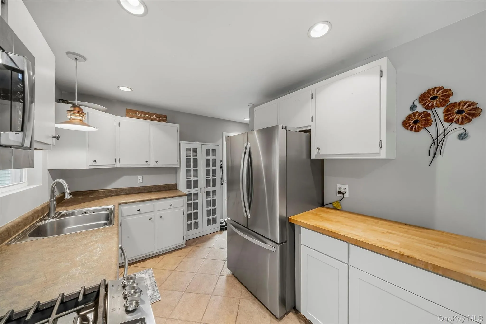 White cabinetry, stainless steel appliances, tiled flooring, wood-finish countertops, and recessed lighting White cabinetry, stainless steel appliances, tiled flooring, wood-finish countertops, and recessed lighting