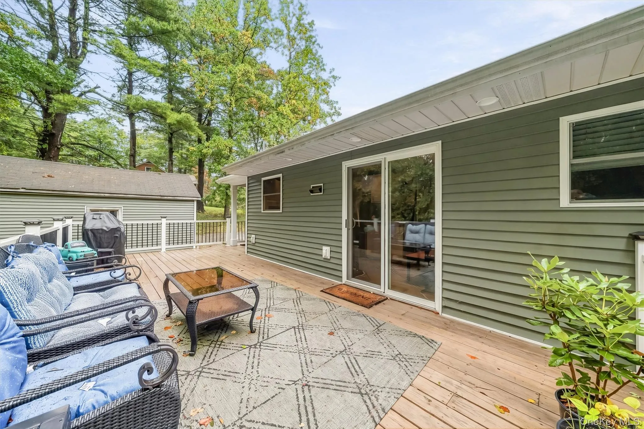 Expansive wood deck with white railing, featuring sliding glass doors and green horizontal siding Expansive wood deck with white railing, featuring sliding glass doors and green horizontal siding