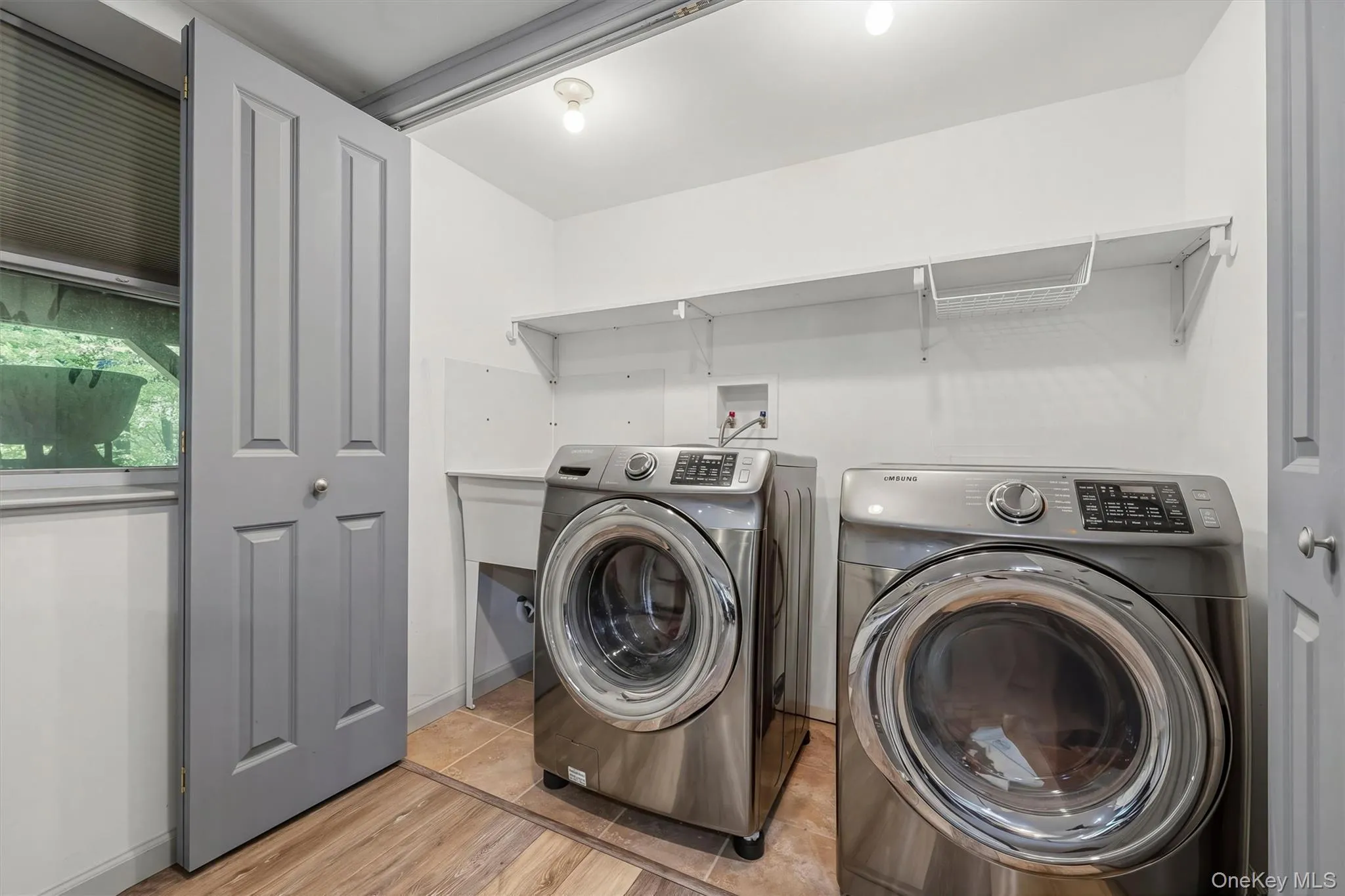 Laundry area featuring wood-finish flooring, white walls, built-in shelving, and utility sink Laundry area featuring wood-finish flooring, white walls, built-in shelving, and utility sink