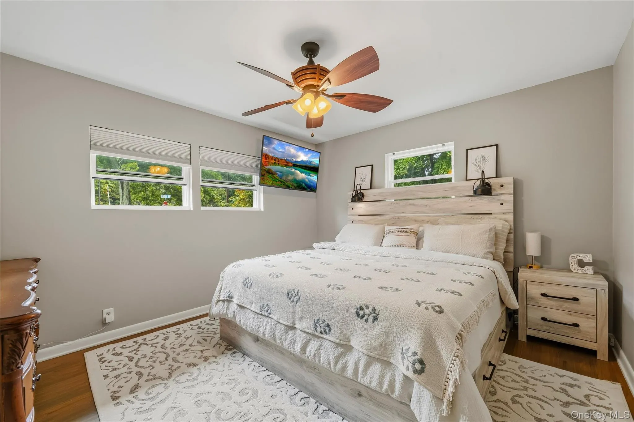 Warm wood-finish flooring, light gray wall paint, multiple windows, and a ceiling fan with light fixture Warm wood-finish flooring, light gray wall paint, multiple windows, and a ceiling fan with light fixture