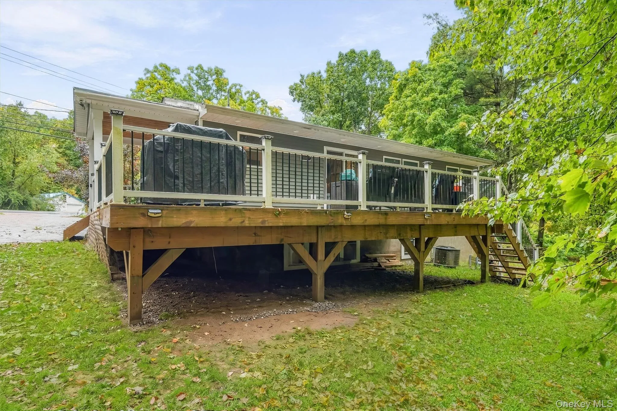 Wood deck with white and black railings, surrounded by mature trees, and featuring a staircase to the ground level Wood deck with white and black railings, surrounded by mature trees, and featuring a staircase to the ground level