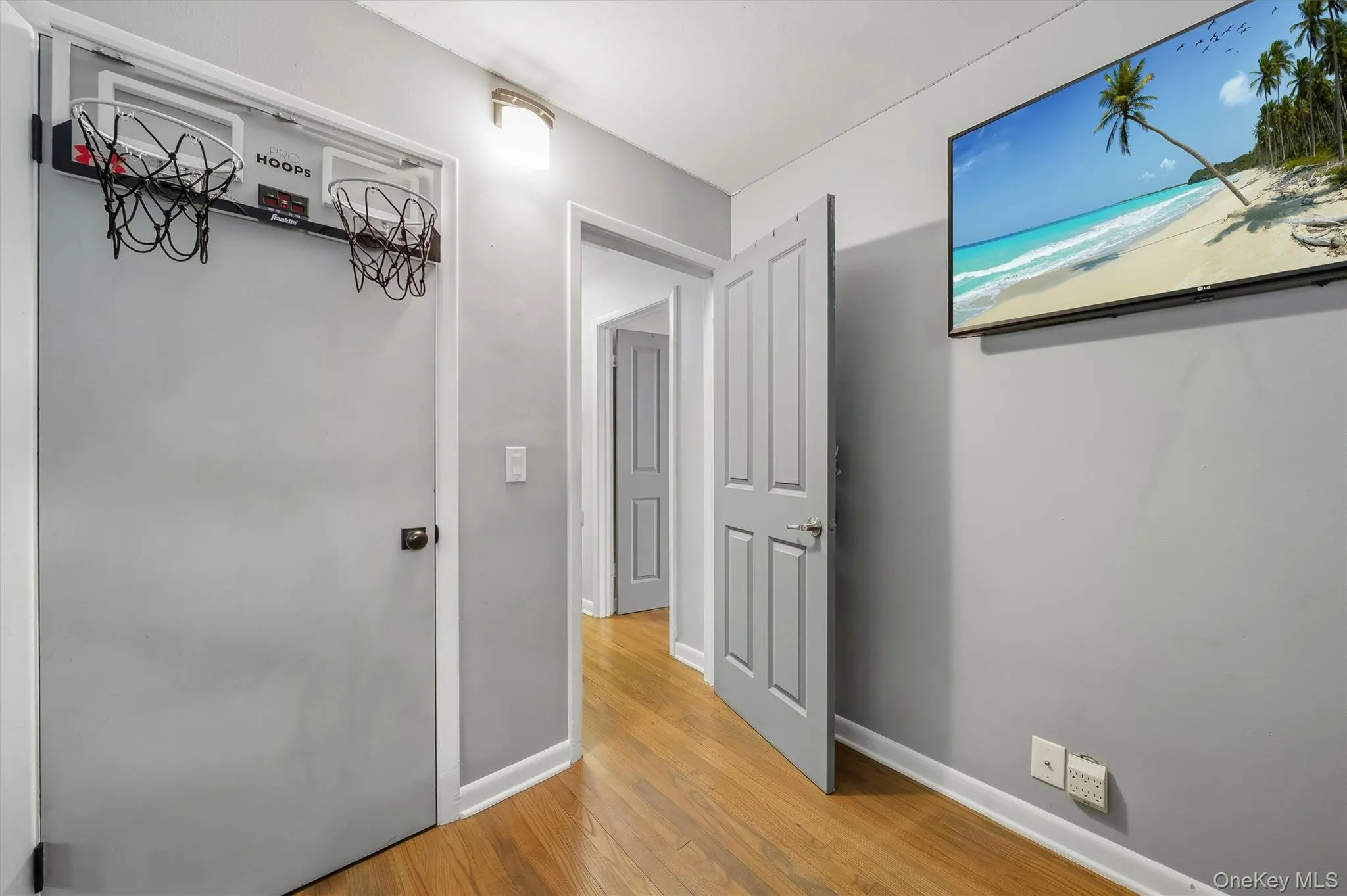 Hallway featuring warm wood-finish flooring, white six-panel doors, and neutral gray walls with recessed lighting Hallway featuring warm wood-finish flooring, white six-panel doors, and neutral gray walls with recessed lighting